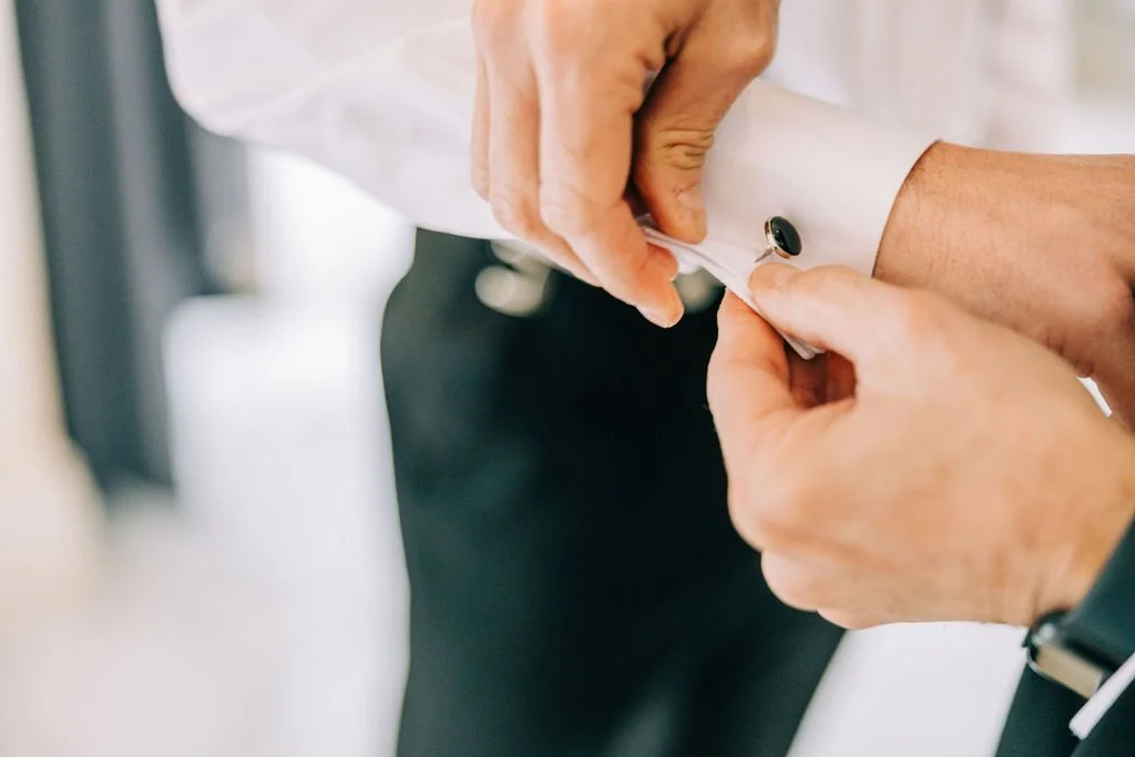 Close-up of a person fastening cufflinks on a white dress shirt sleeve.
