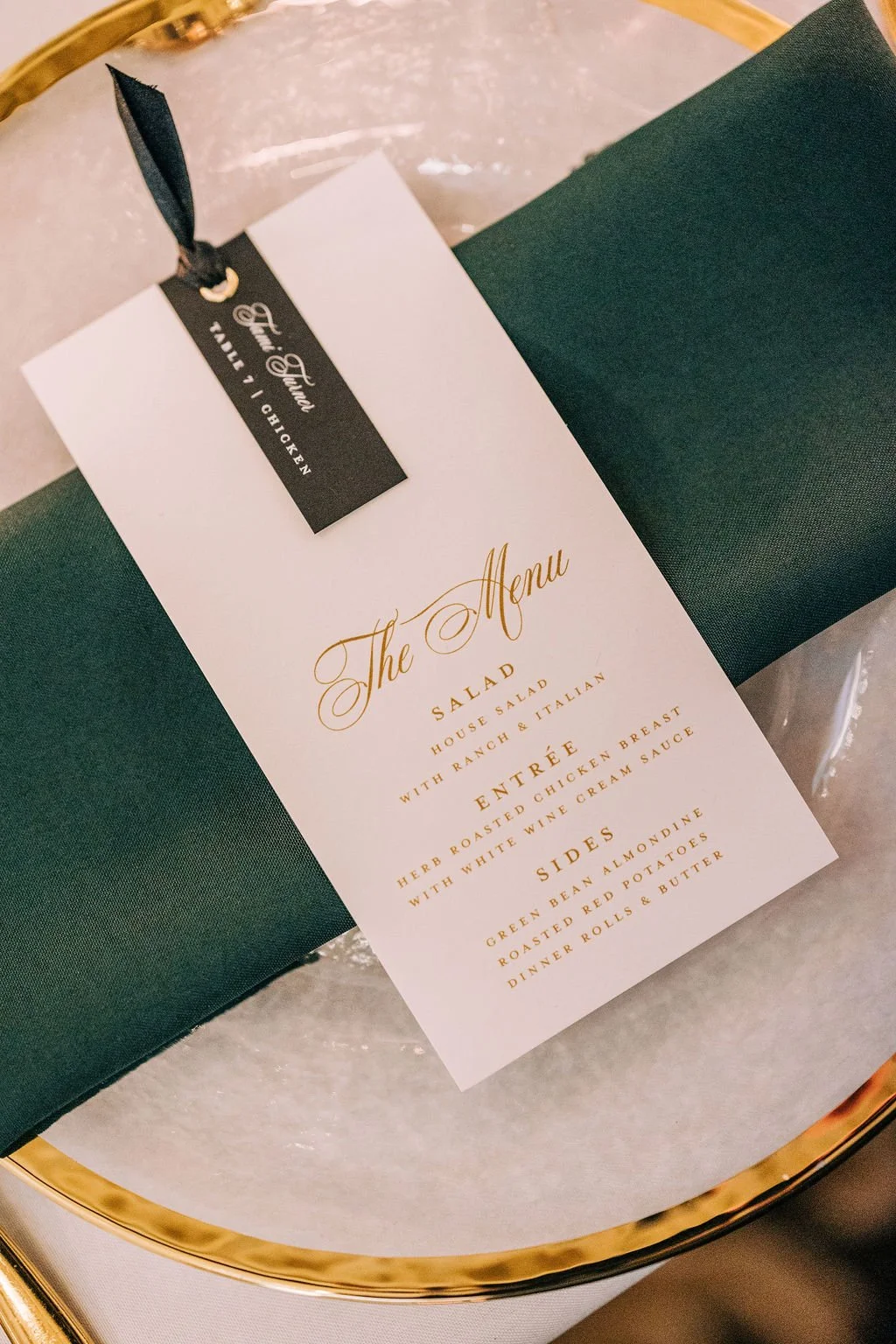 Elegant event menu card on a table setting with gold-rimmed plate and green napkin, featuring salad, entrée, and sides options.