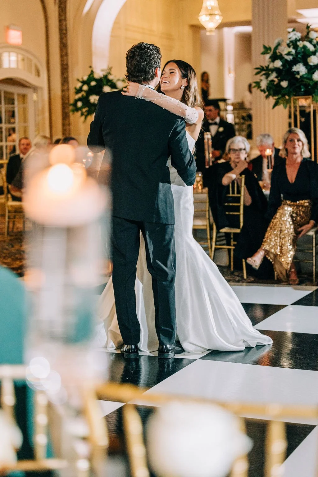 Bride and groom having their first dance at a wedding reception with guests watching in the background.