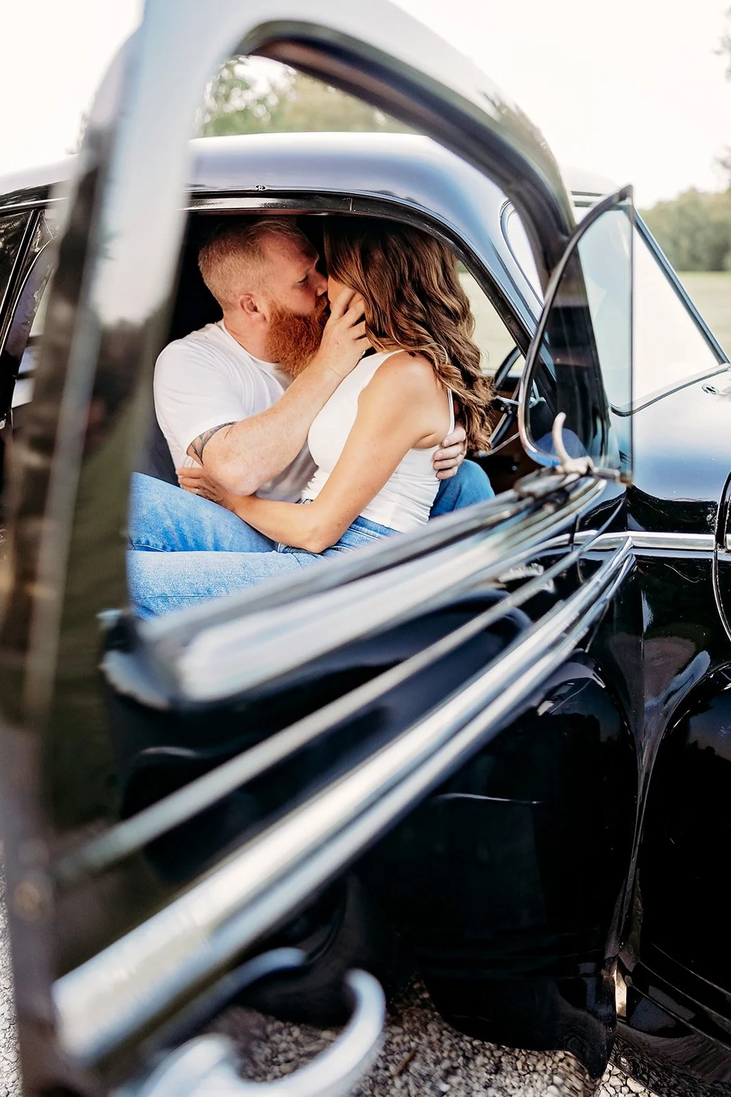 A couple kissing inside a vintage car with an open door.