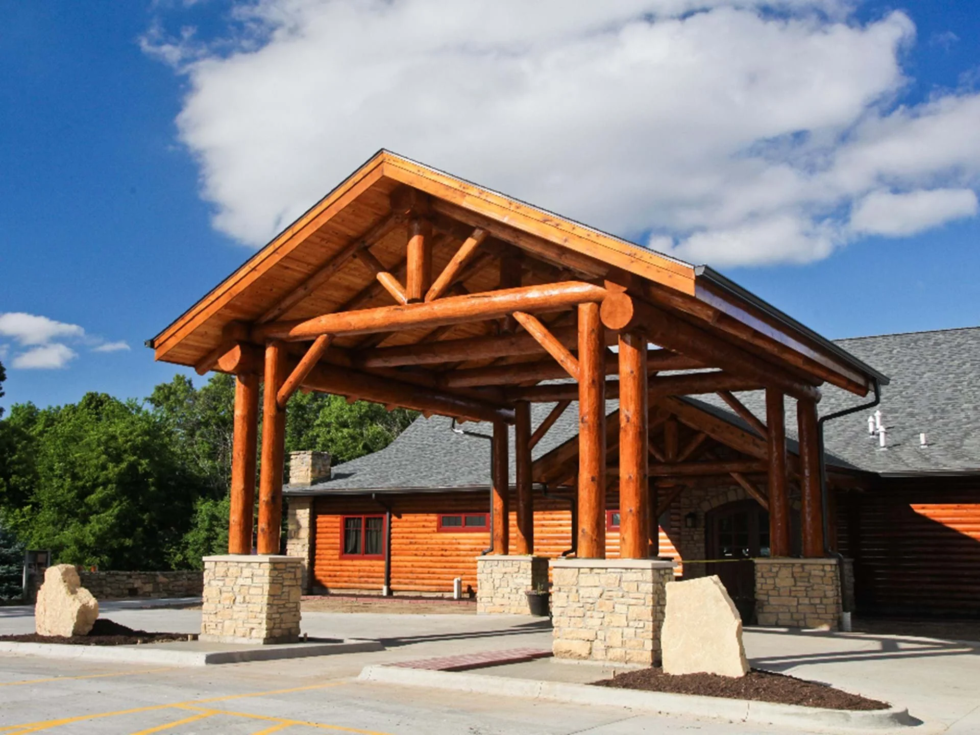 Wooden cabin with large log structure at entrance, surrounded by trees and blue sky