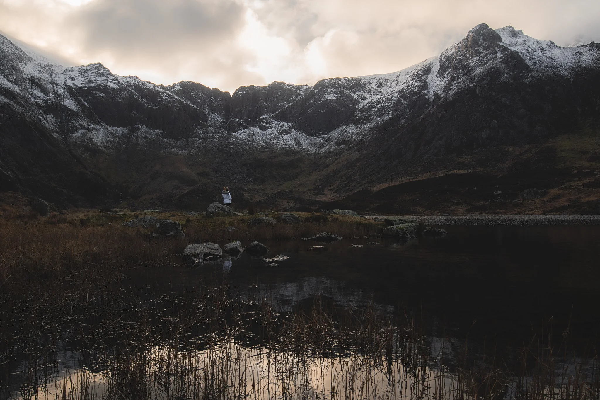 Person sitting on a rock near a mountain lake with snow-capped peaks in the background