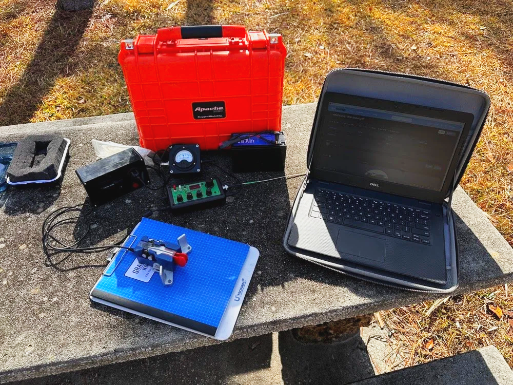 Penntek TR-35 QRP transceiver with Dell laptop, CW paddle key, and logbook on picnic table at POTA activation