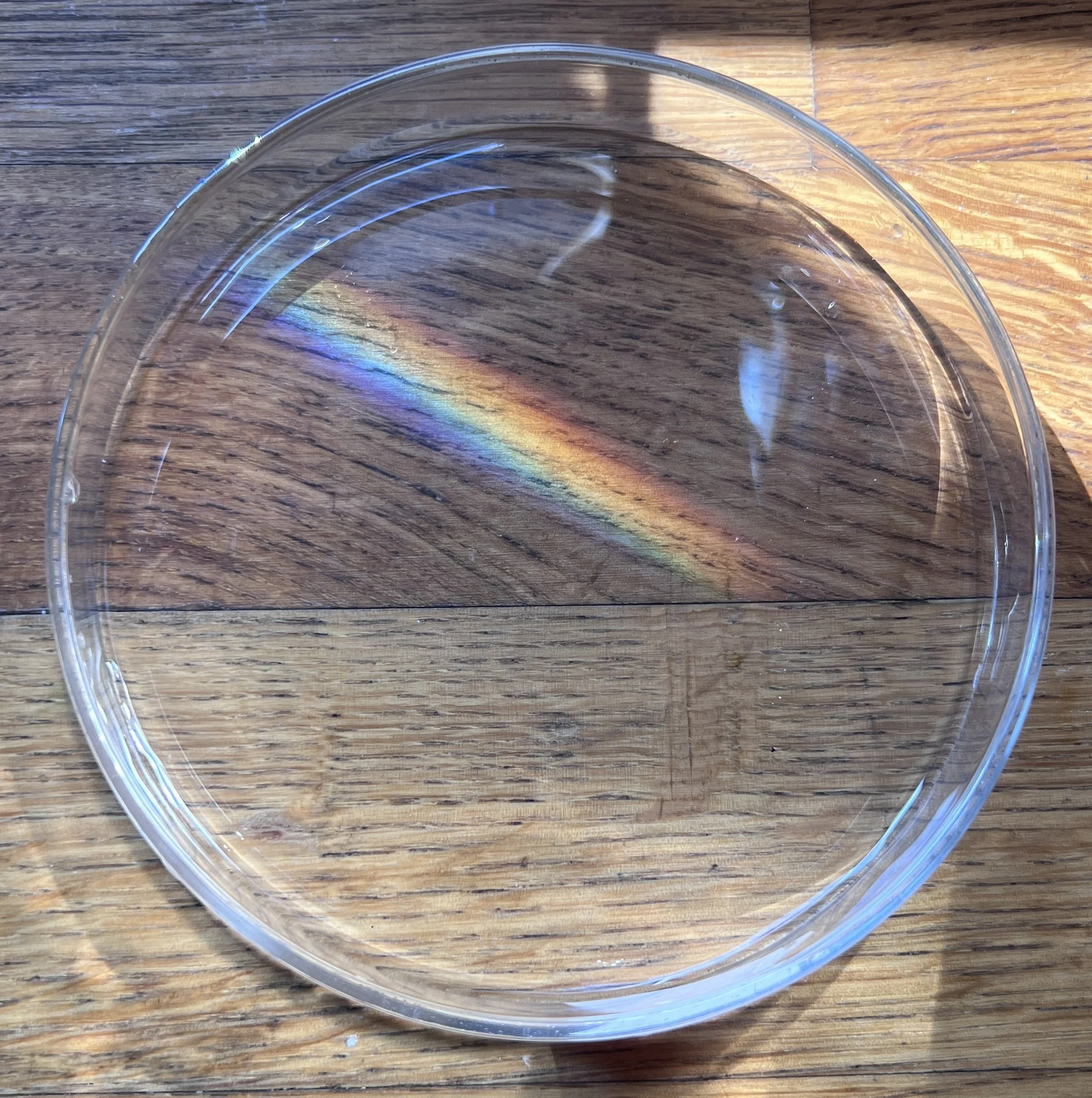 Close-up of a clear glass bowl on a wooden surface, with rainbow-like reflections.
