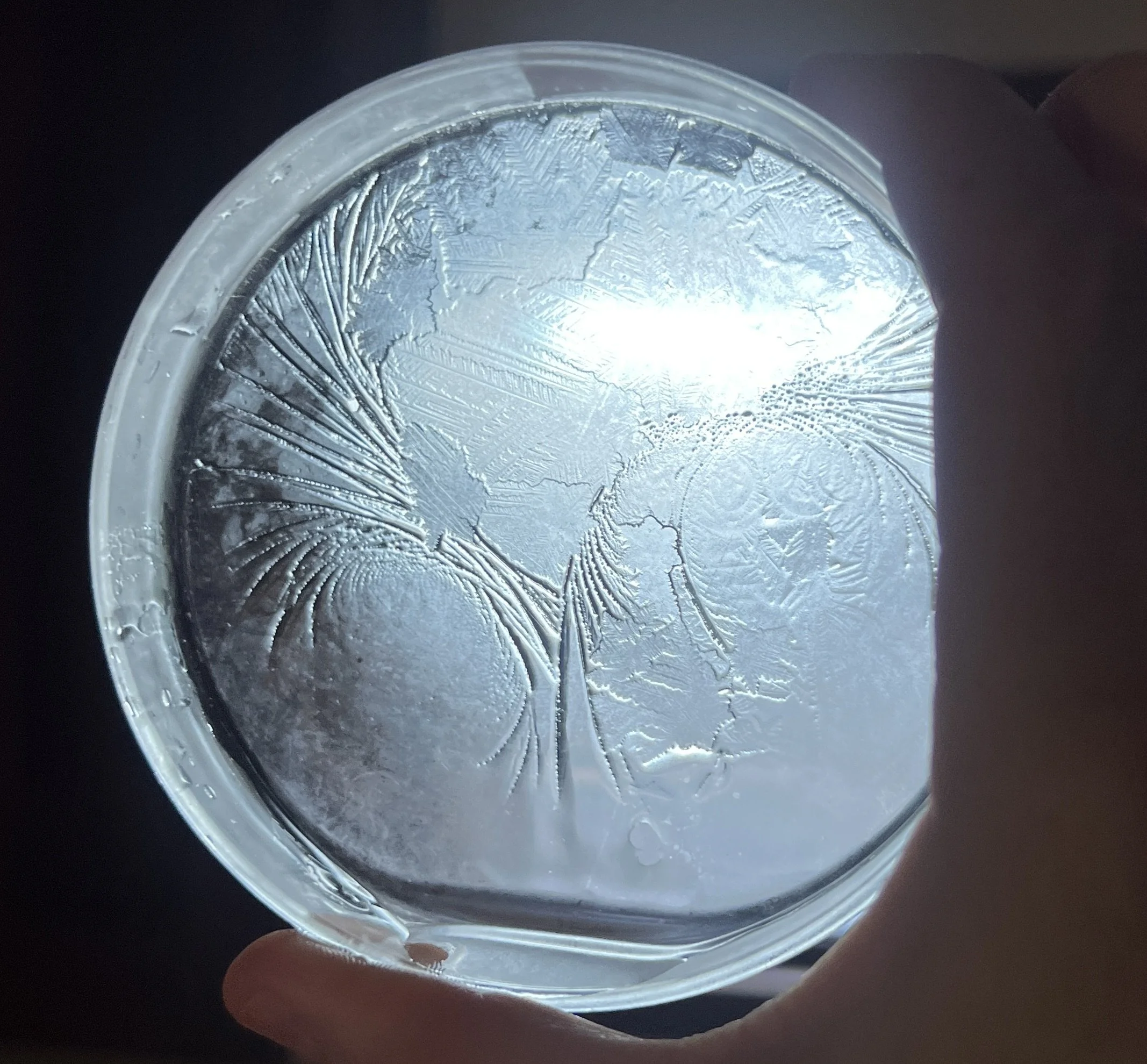Close-up of a transparent glass with ice, held by a person's hand, showing frost on the surface and cracks in the ice.
