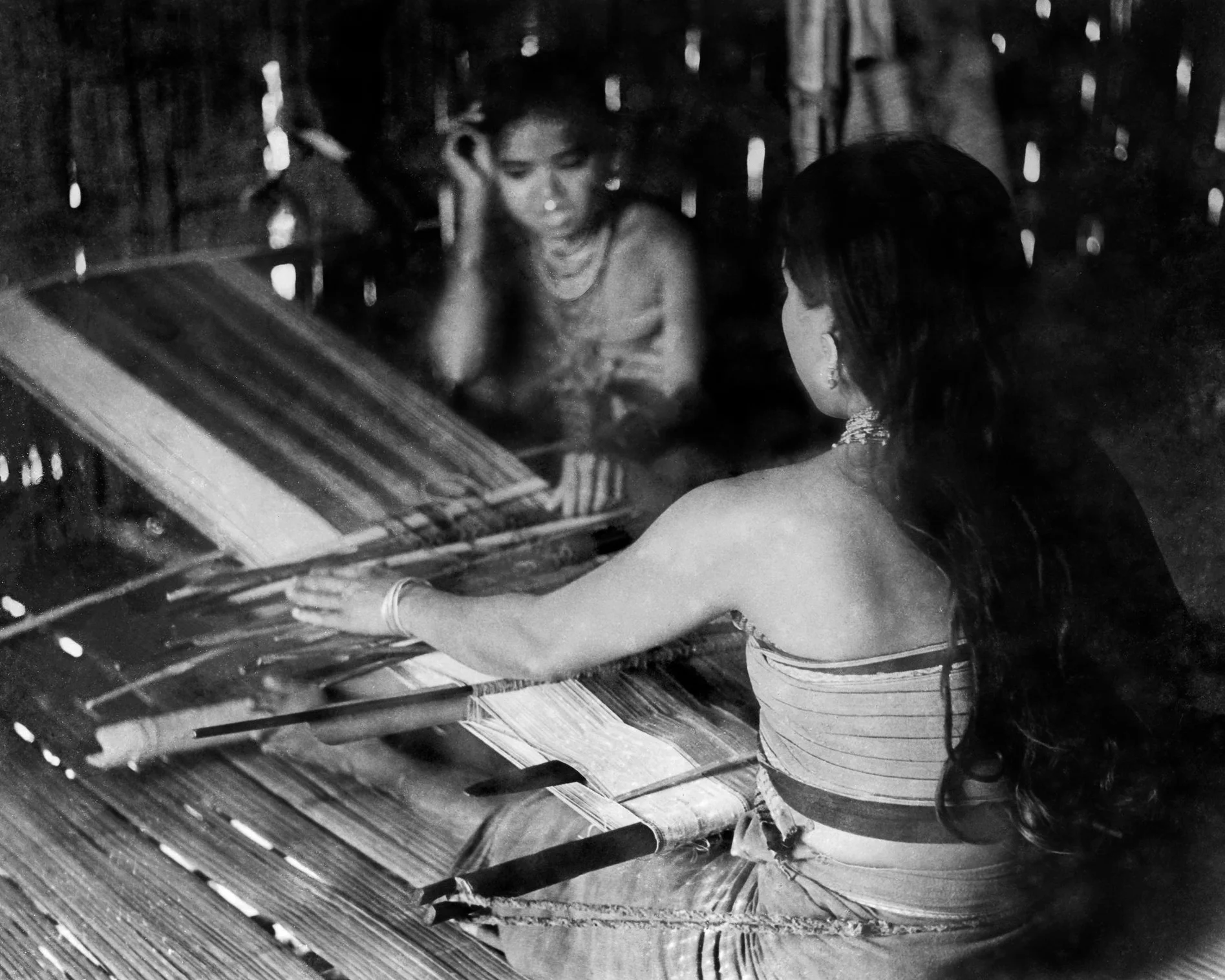 Tripuri woman weaving one half of a Rignai (traditional wrap skirt) with a white border on a ri thanti , or backstrap loom. c.1974