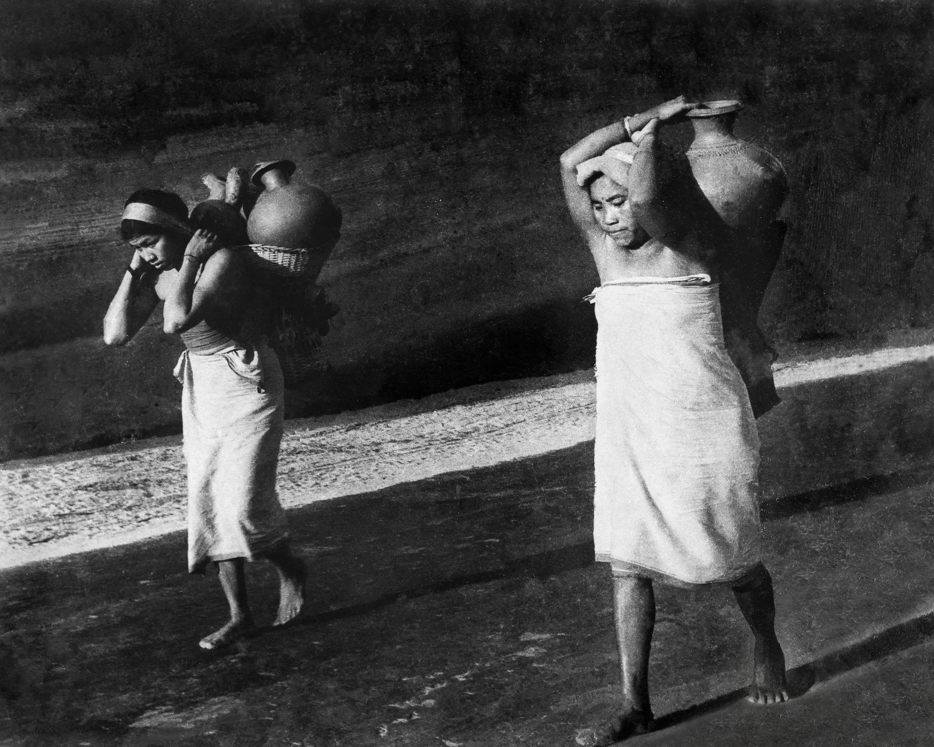 Women from the Deb Barma tribe wearing simple white pasras (wrapped lower garment) carrying water back in clay pots to their village near Teliamura. c.1977