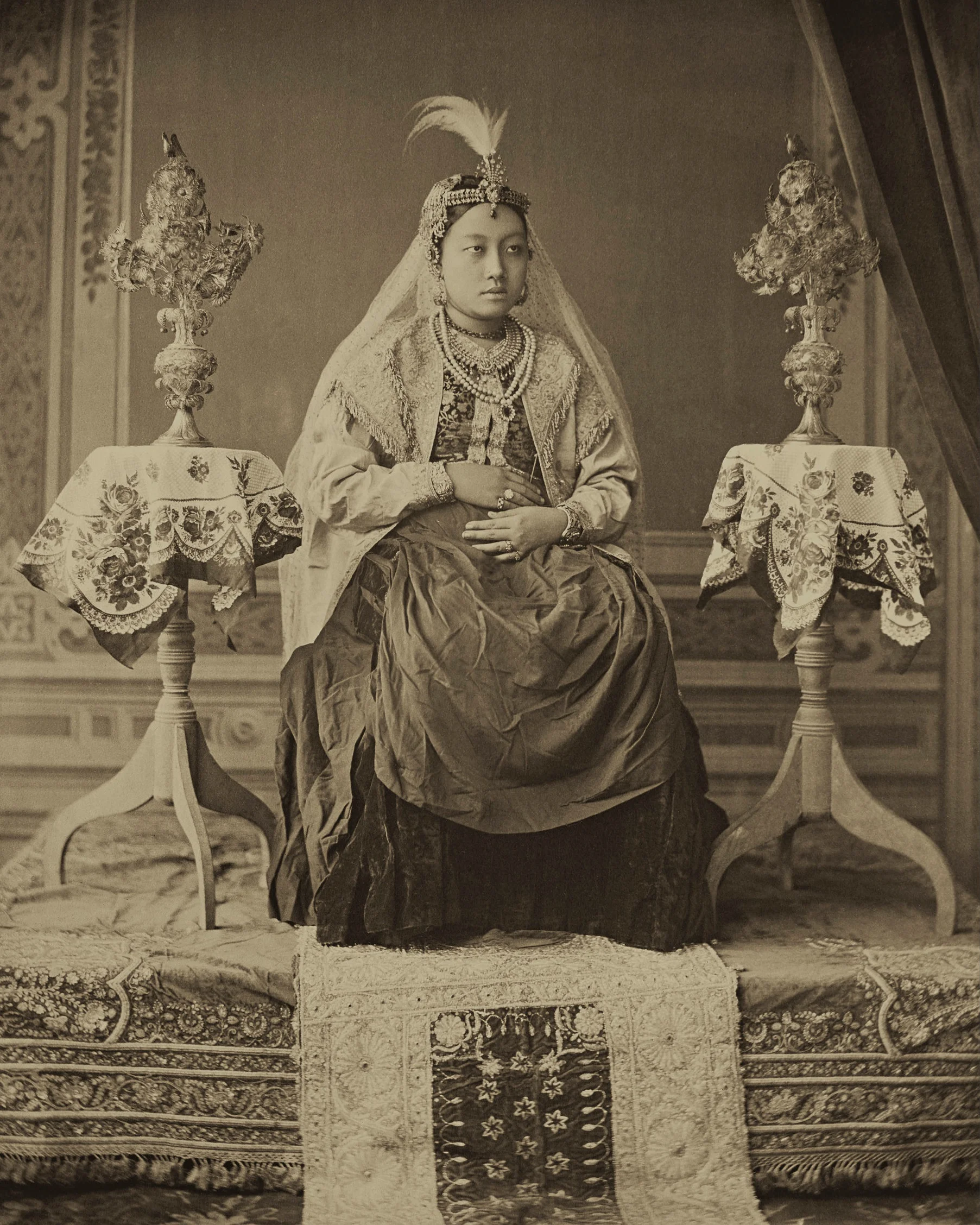 Maharani Monmohini Devi. The Maharani posing like British Queen Victoria in what appears to be an eclectic and creatively staged shot. The Queen wears a plain European dress with one of her own blouses, a silk jacket with long sleeves and a feathered Mughal head ornament that holds a veil down in place. c.1890. Photographed by Raja Bir Chandra Manikya. Platinum palladium print.