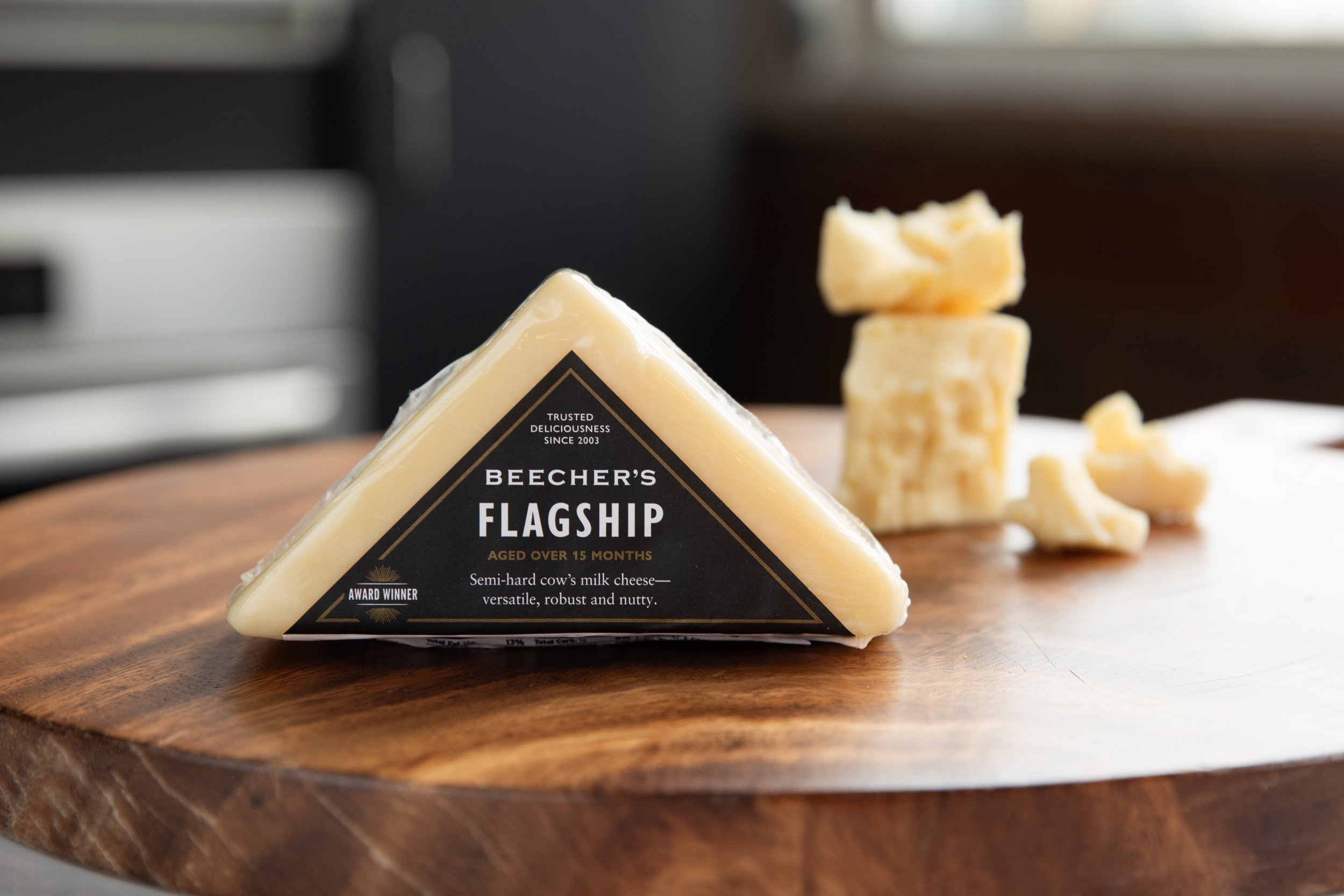 A wedge of Beecher's Flagship semi-hard cow's milk cheese on a wooden surface with a stack of cheese pieces in the background.