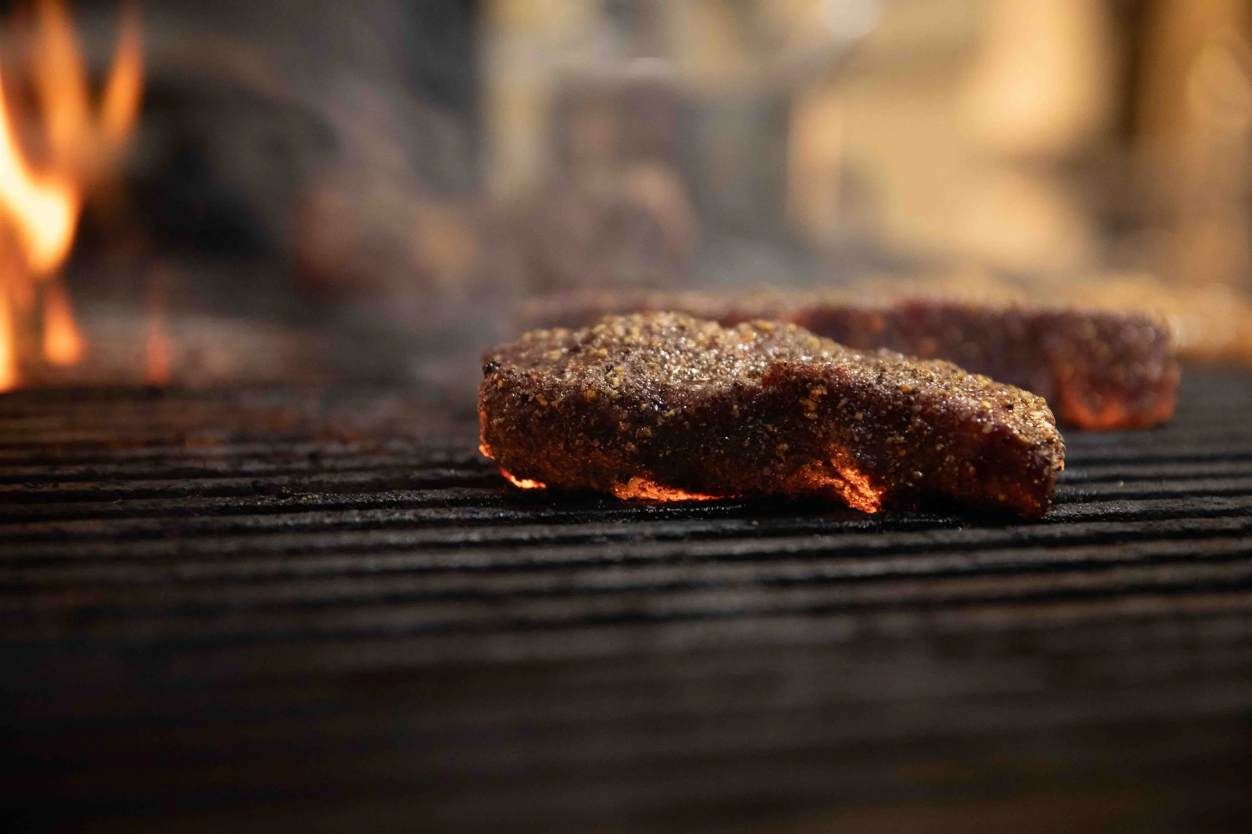 Meat cooking on a grill with visible flames and hot coals underneath.