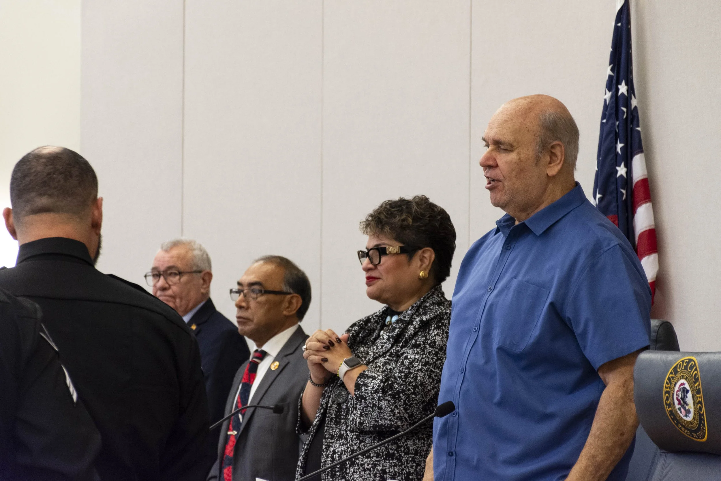 Town president Larry Dominick sits flanked by Cicero trustees during a public board meeting, with some looking at the resident speaking and others looking down.