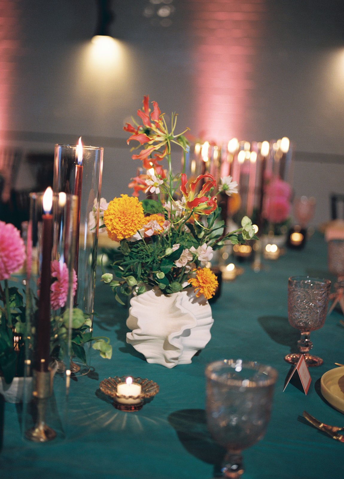 Close-up of a decorated dining table with a floral centerpiece, candles, and elegant glassware in a dimly lit setting.