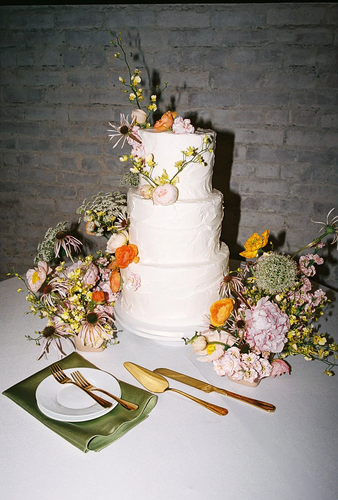 White wedding cake styled with colorful garden-inspired florals and surrounding floral arrangements by Elizabeth McKenzie Florals.