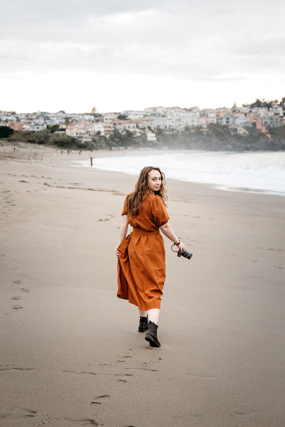  brand portrait of photographer Toni Toscano walking away from camera and holding her Olympus camera in hand, shot at Baker Beach in San Francisco by brand photographer Allison Busch Photography 