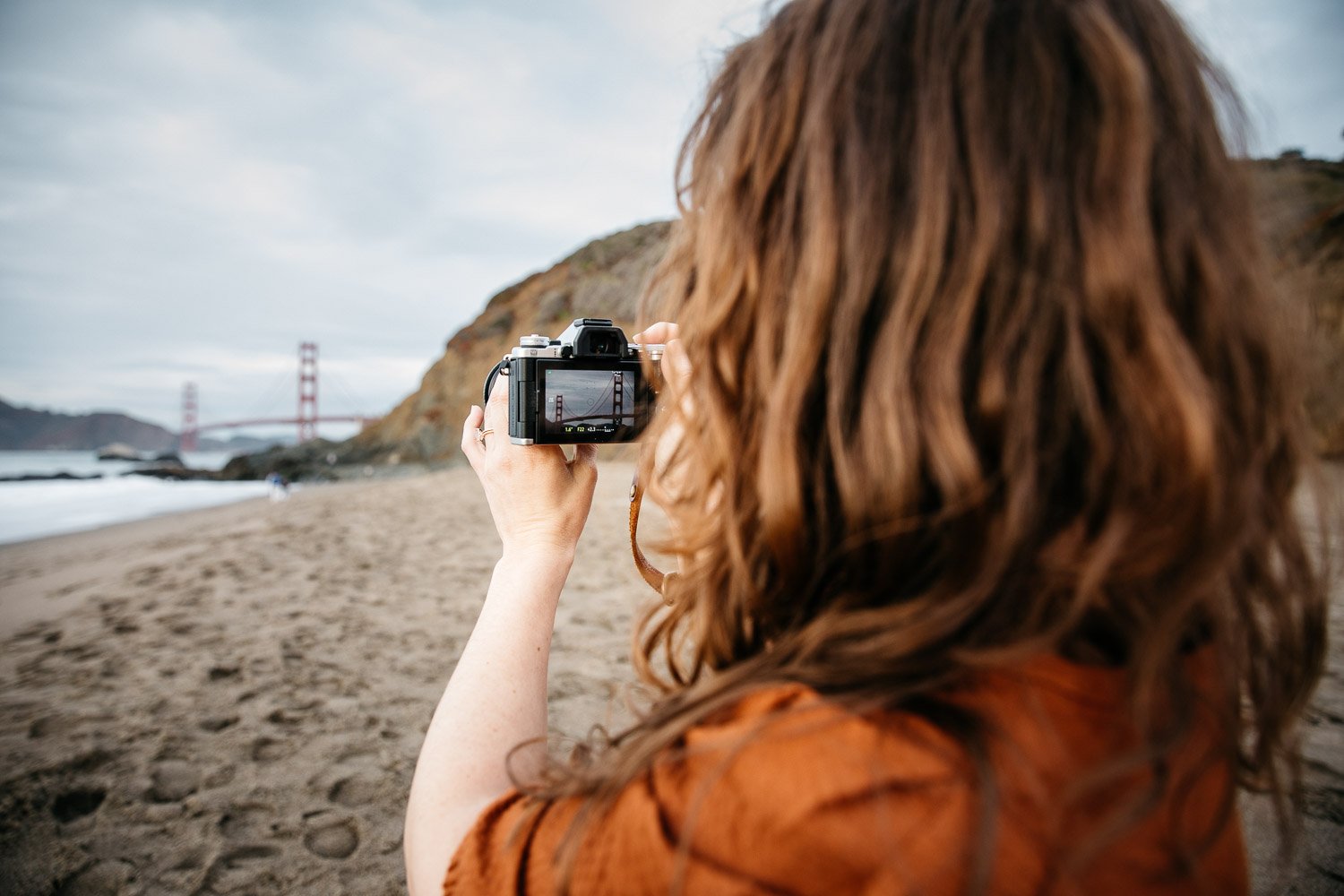  brand photograph of photographer Toni Toscano taking a picture of the Golden Gate Bridge which looms in the background, shot at Baker Beach in San Francisco by brand photographer Allison Busch Photography 