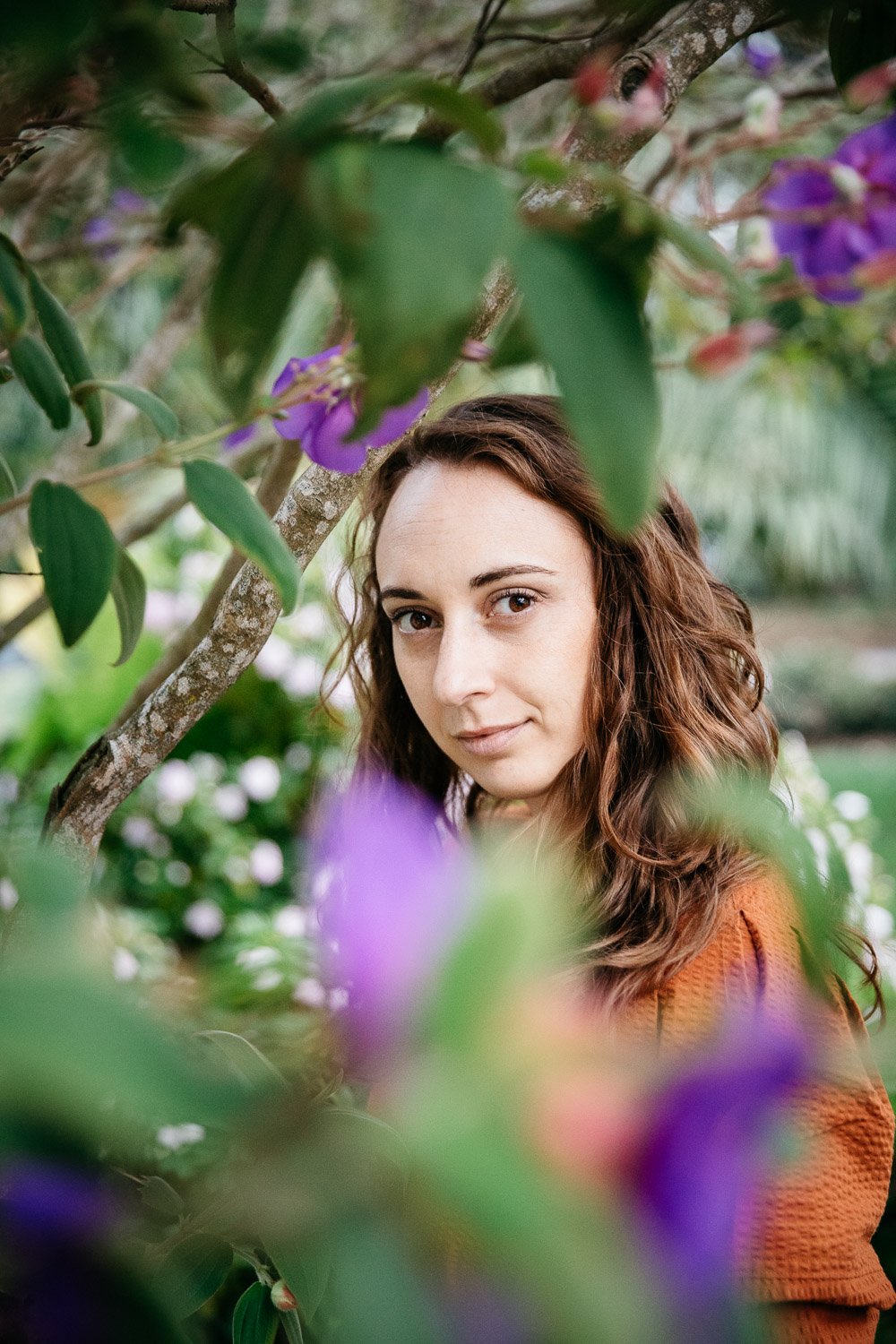  brand portrait of photographer Toni Toscano looking at camera and shot through tree with purple flowers, shot in the Presidio in San Francisco by brand photographer Allison Busch Photography 