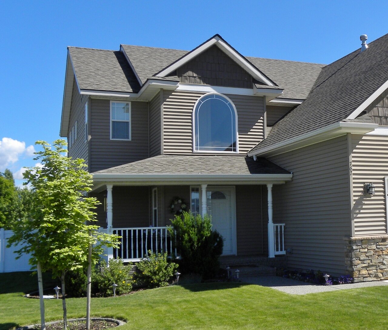  Newer tan, two-storied home with porch and lawn. 