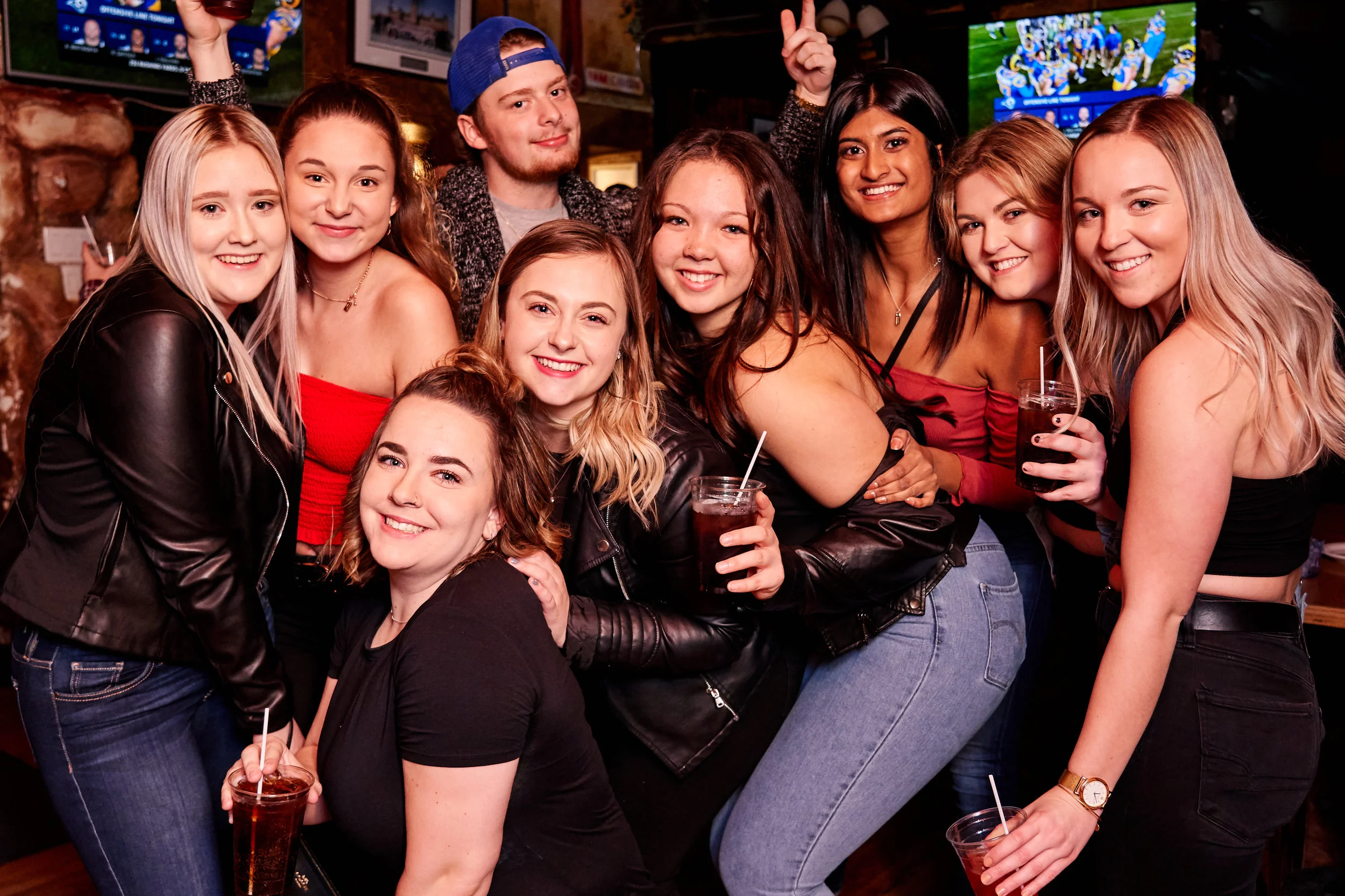 Group of young friends smiling and celebrating at a bar, holding drinks.
