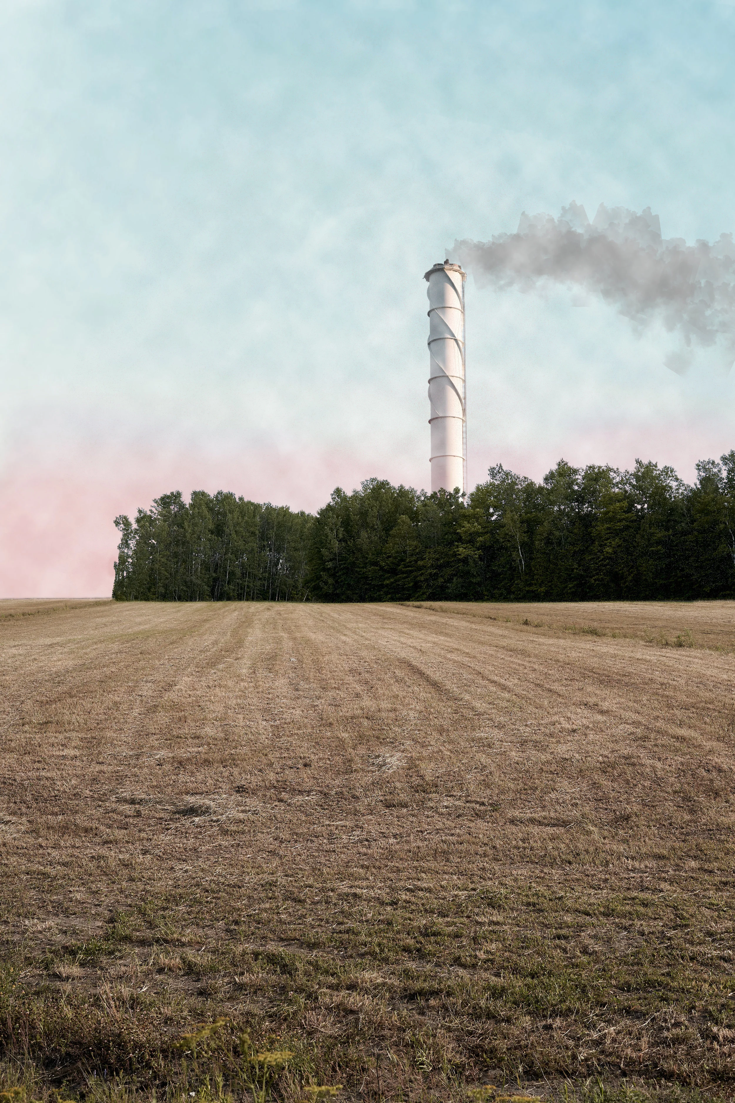 A rural landscape with a dry, harvested field in the foreground, a line of trees in the middle ground, and a tall industrial smokestack emitting gray smoke in the background under a pastel sky.