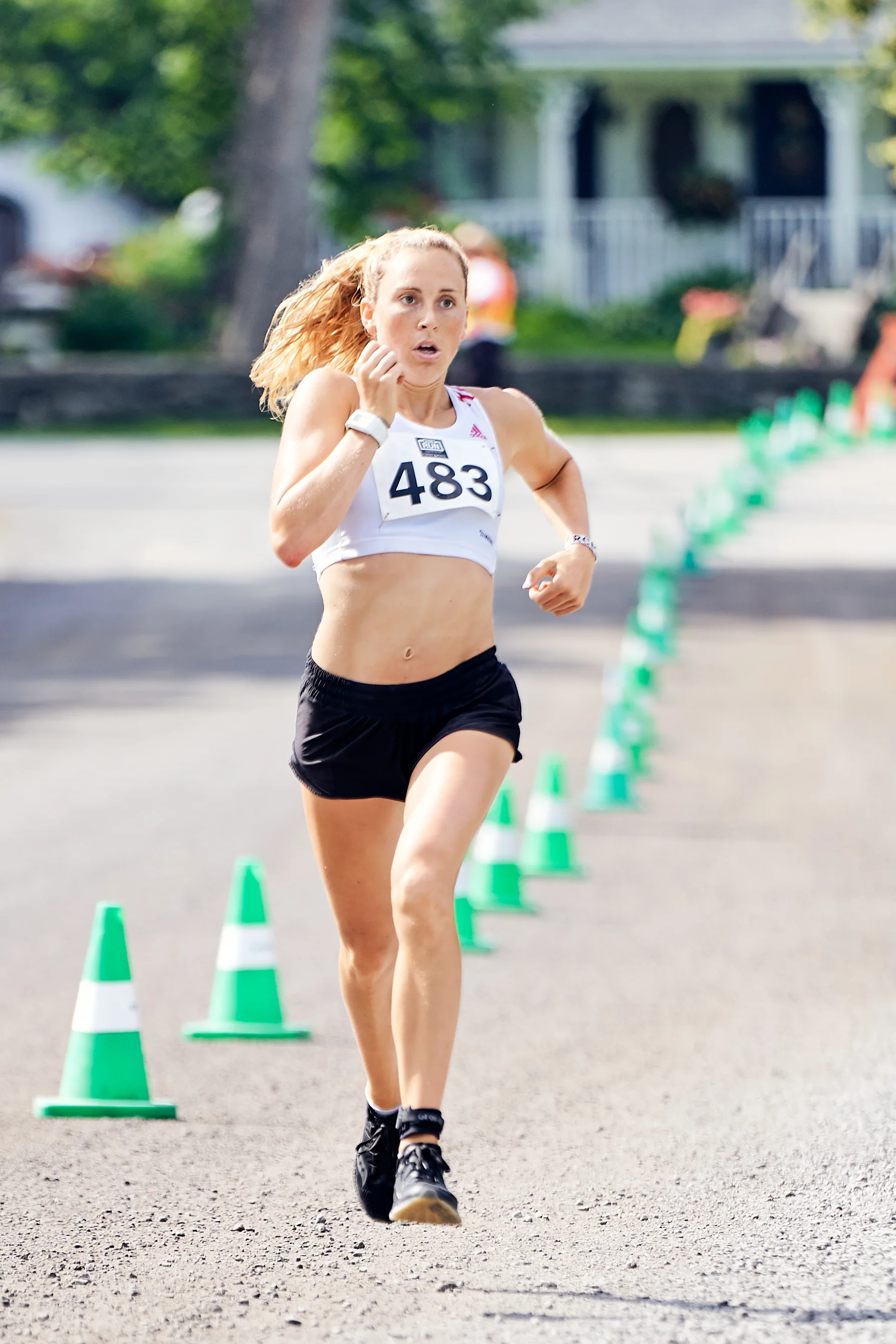 A female runner with bib number 483 running on a road marked with green and white traffic cones.