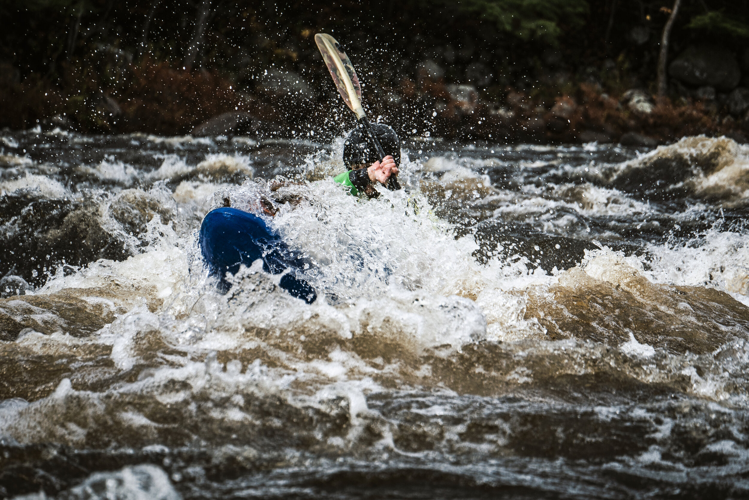 Person kayaking through rough whitewater rapids, wearing a helmet and a green jacket.