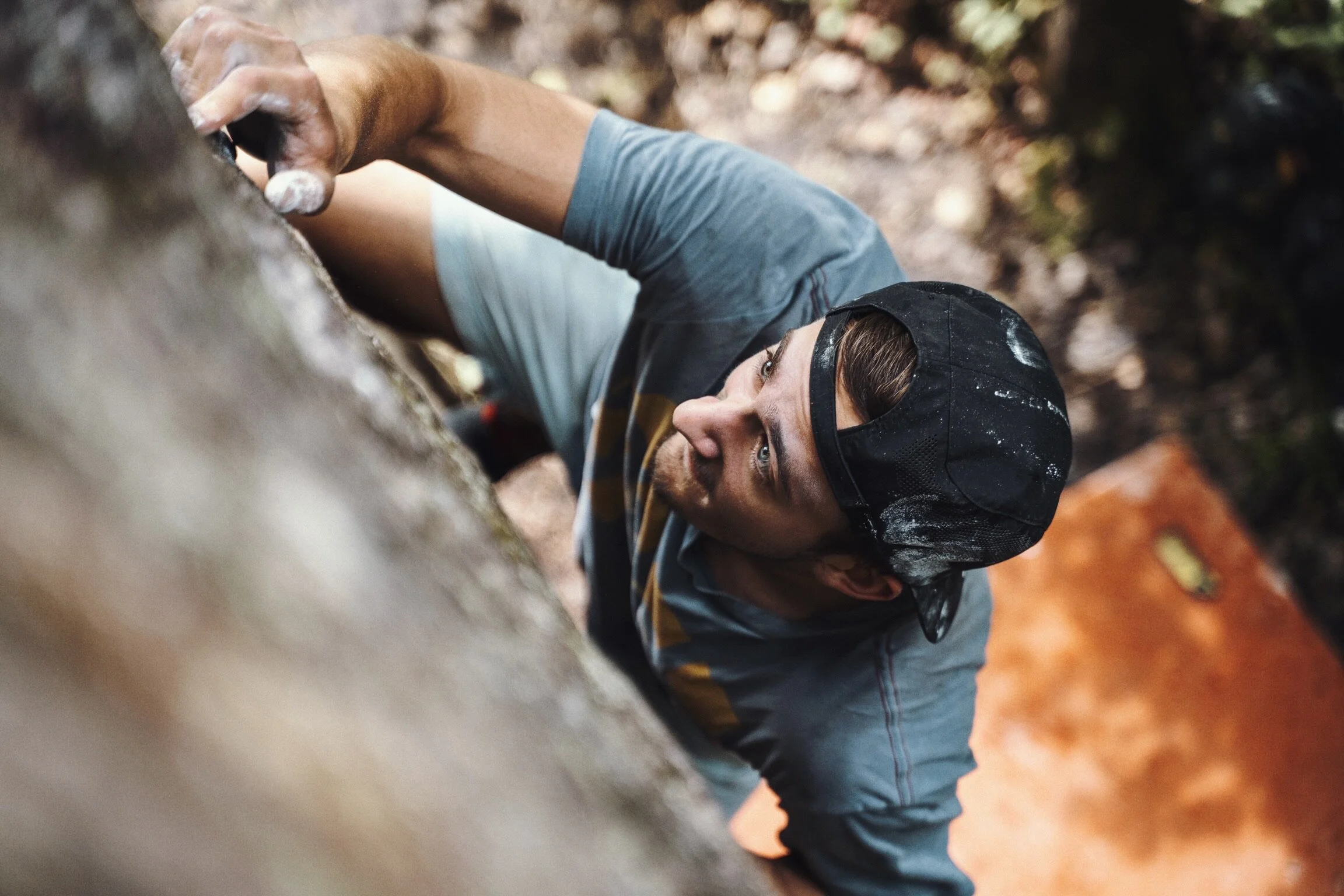 A man with a baseball cap climbing a rock wall outdoors.