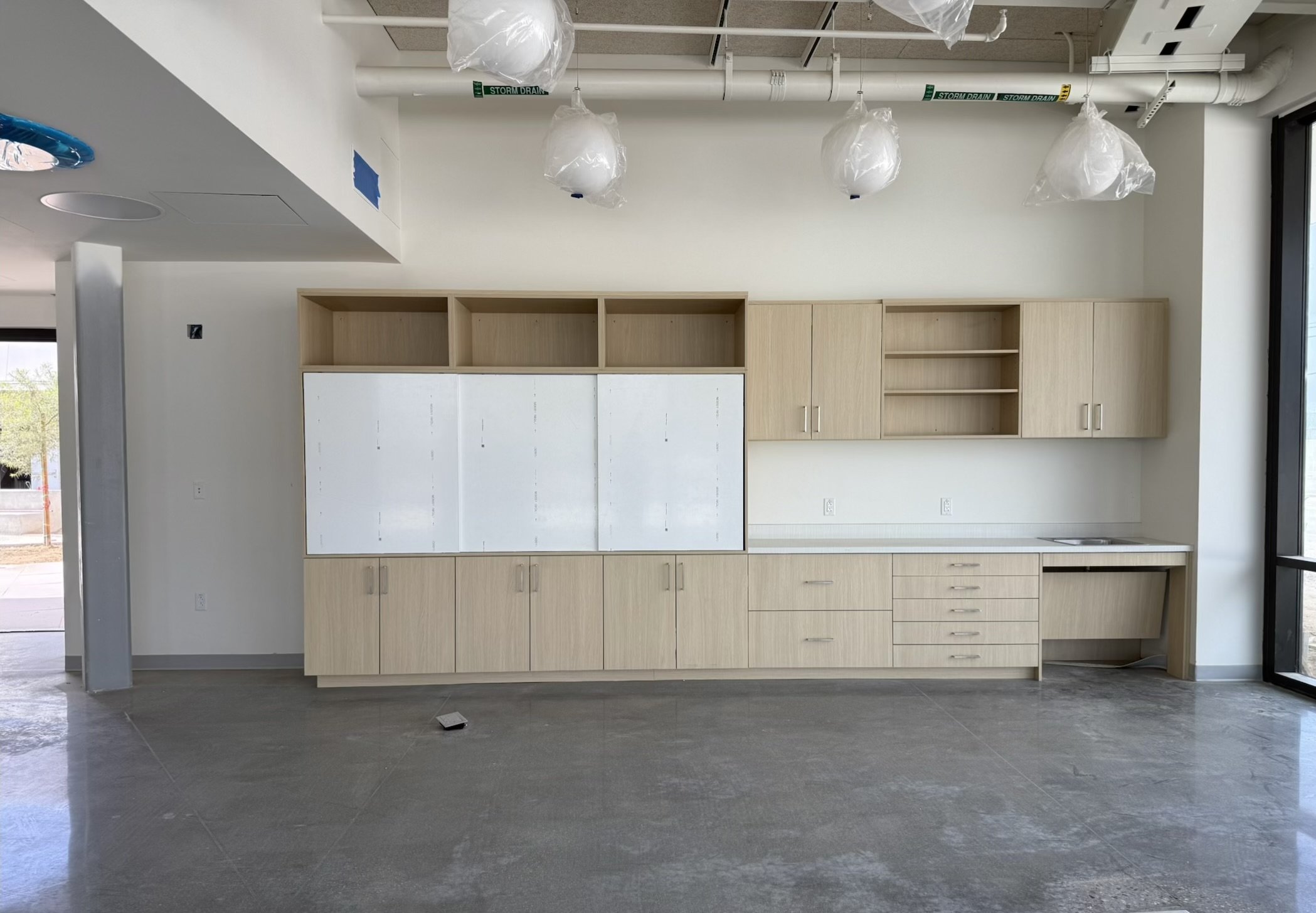 Custom rift-cut white oak classroom storage wall with whiteboards, upper cabinets and sink counter, installed in a Redondo Beach private school