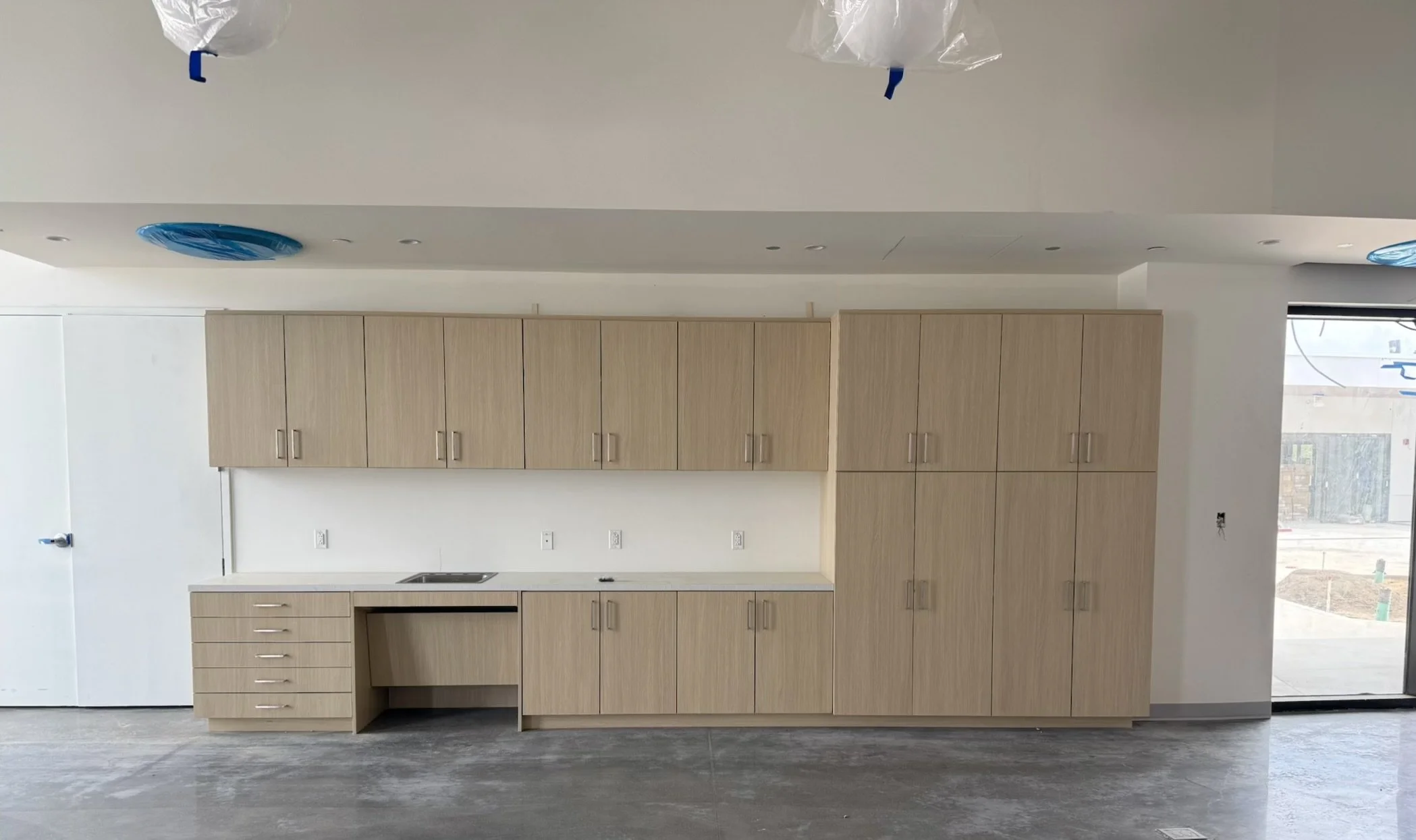 Rift-cut white oak built-in casework with tall storage cabinets, base drawers and an integrated sink counter in a Redondo Beach school
