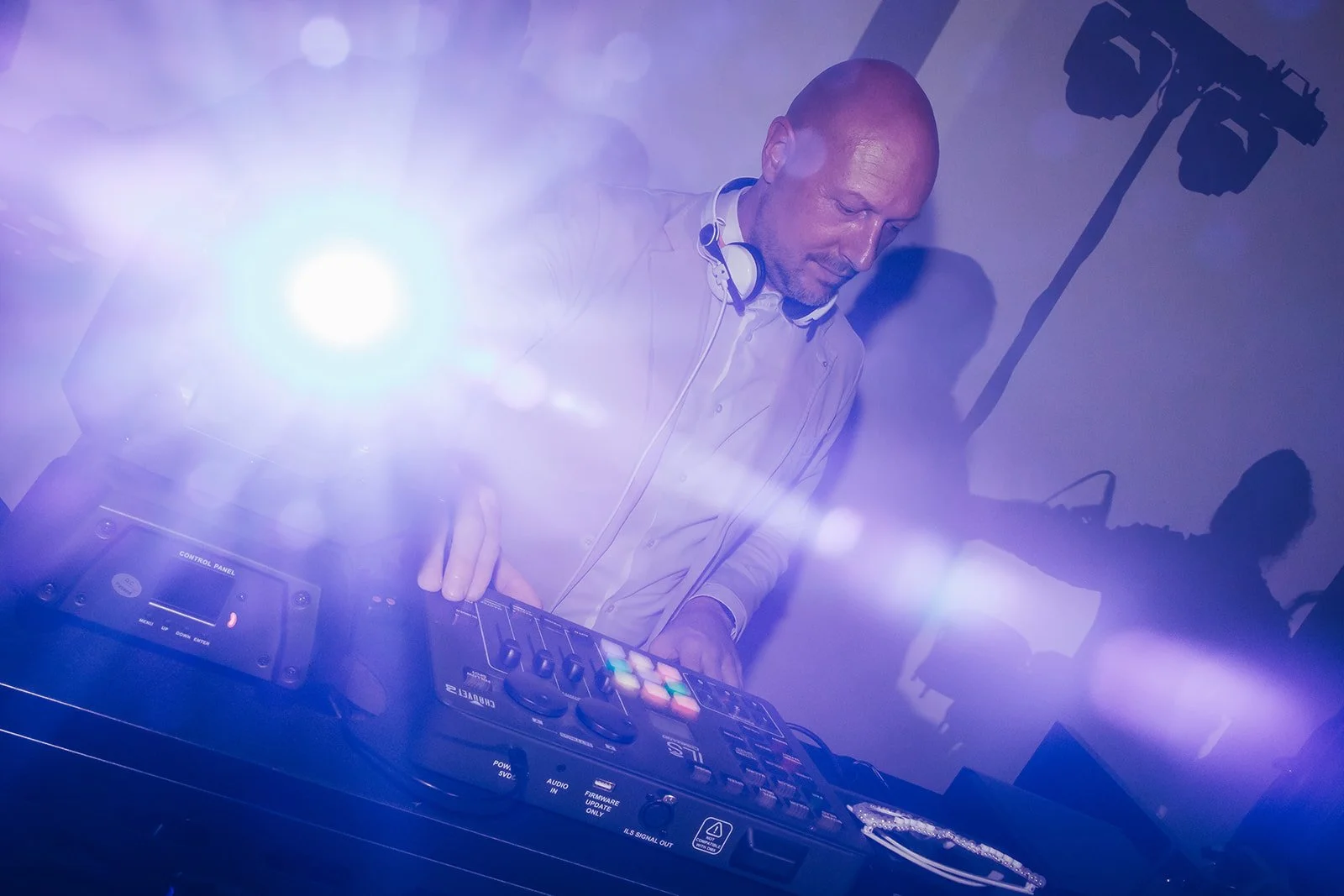 DJ Marlon konzentriert am Mischpult, mit Kopfhörern um den Hals und violettem Partylicht im Hintergrund.