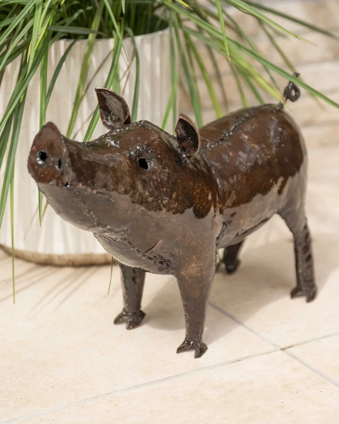 a recycled metal pig garden ornament sat on stones on the beach with the sea in the background