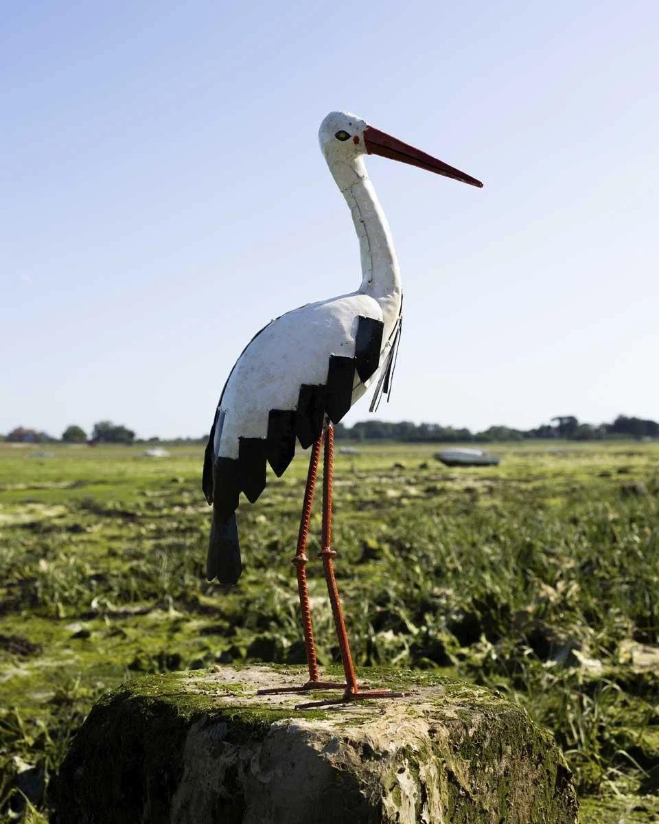 white and orange painted stork sculpture on the shoreline with blue sky