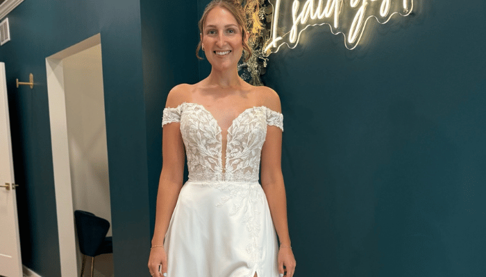 Bride wearing an off-the-shoulder lace wedding dress with a plunging neckline during a bridal boutique appointment.