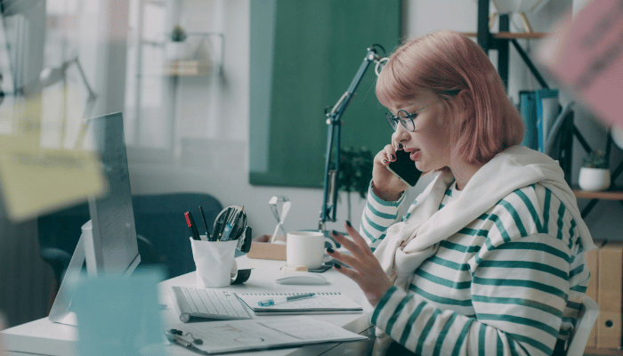 A woman reviewing wedding plans and expenses at a desk while speaking on the phone.