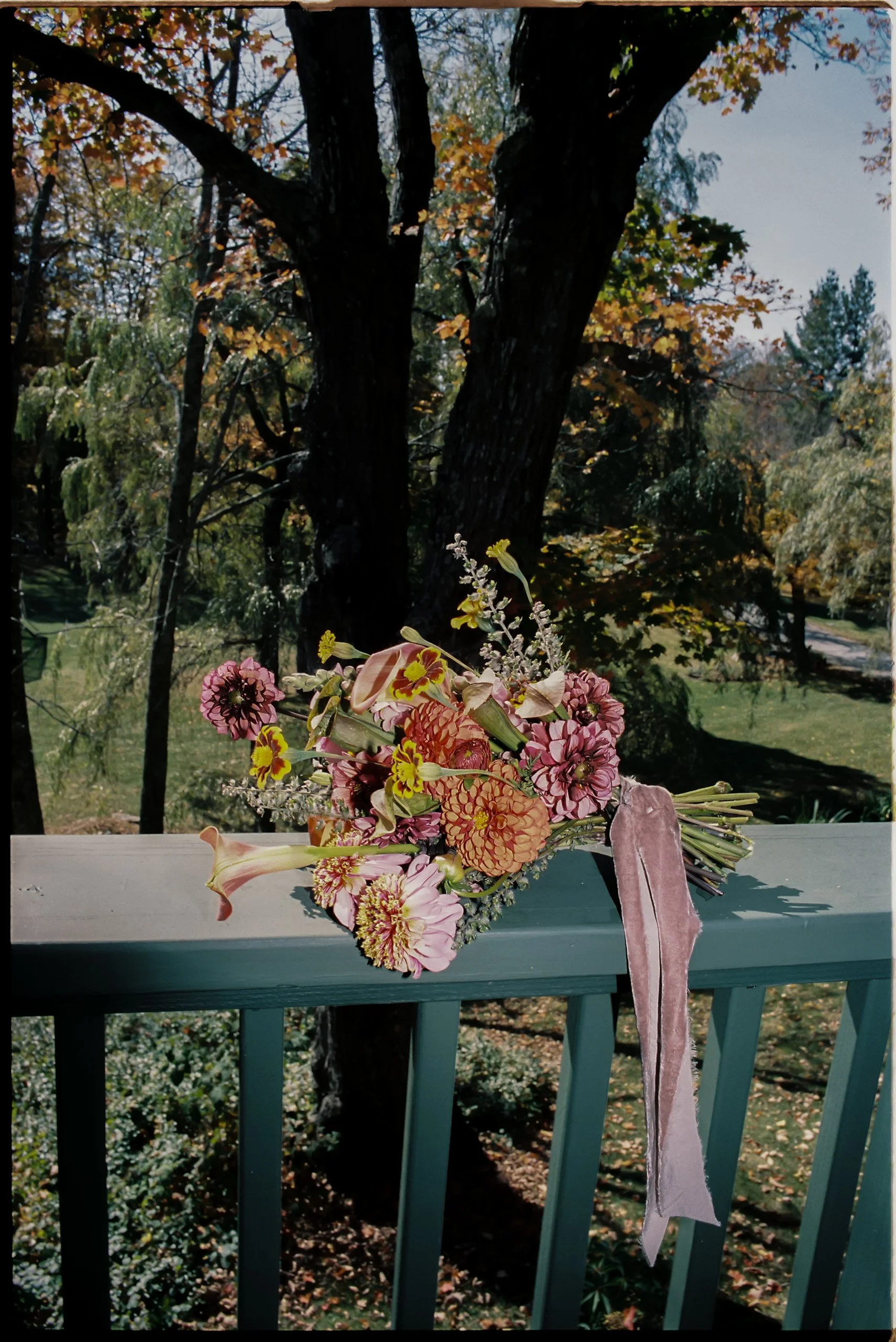 Loose fall wedding bouquet in warm pinks and golds with trailing silk ribbon, styled against wooded mountain views