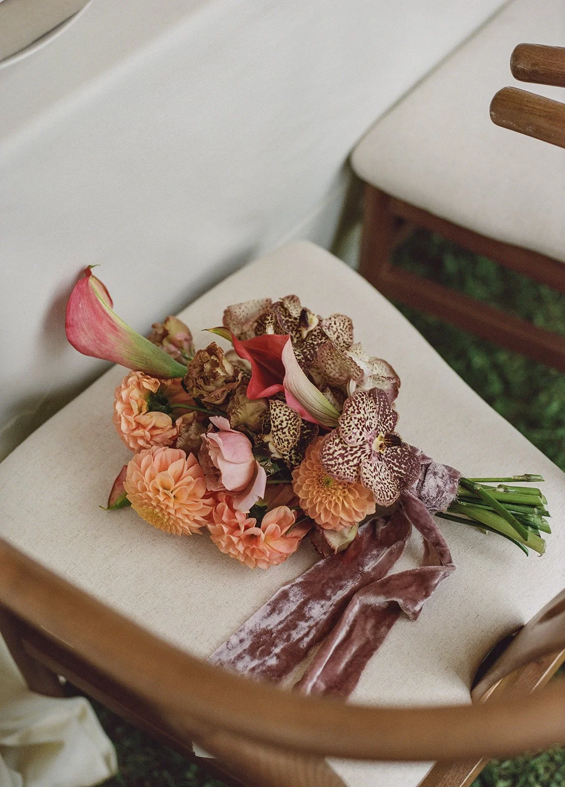Bridal bouquet with peach calla lilies, dahlias, and trailing silk ribbon resting on a chair