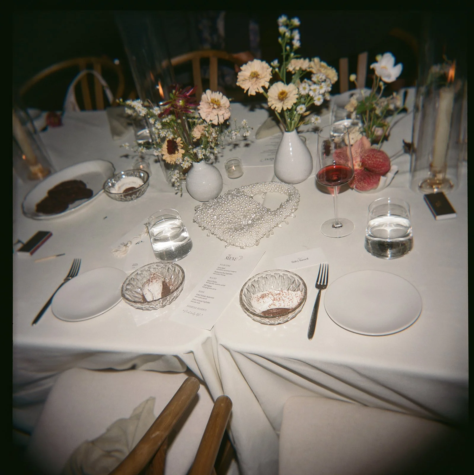 End-of-night table scene with scattered petals, glassware, and softly fading candlelight