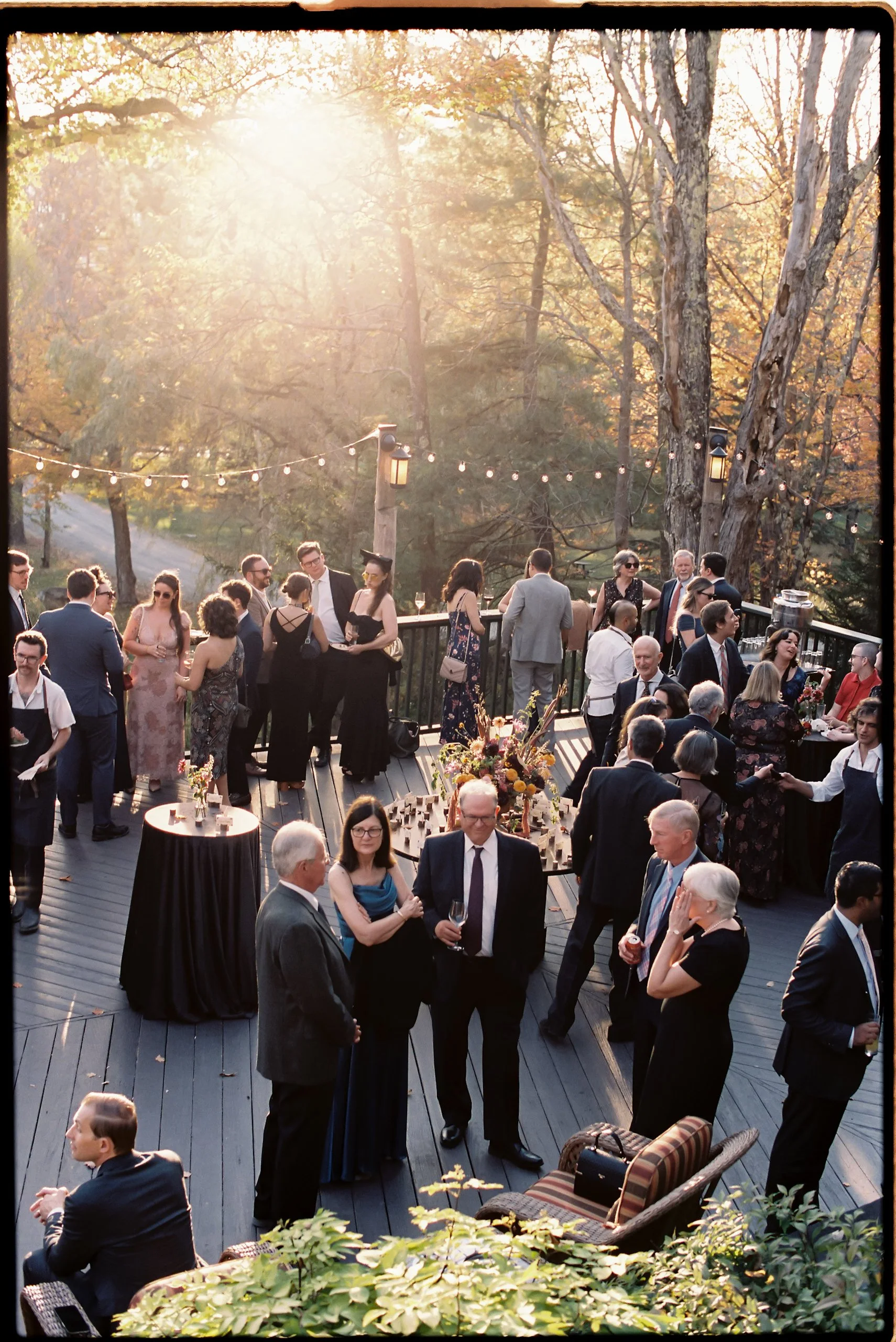 Guests mingling at sunset surrounded by floral-accented cocktail tables and warm fall arrangements