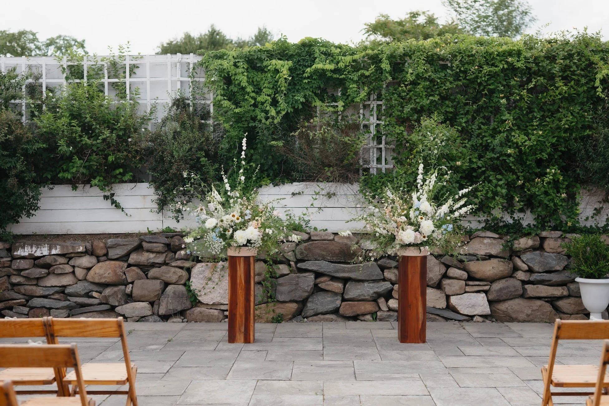  Two wooden pillars with two show stopping flora designs featuring seasonal white blossoms, and trailing greenery to mark the altar   