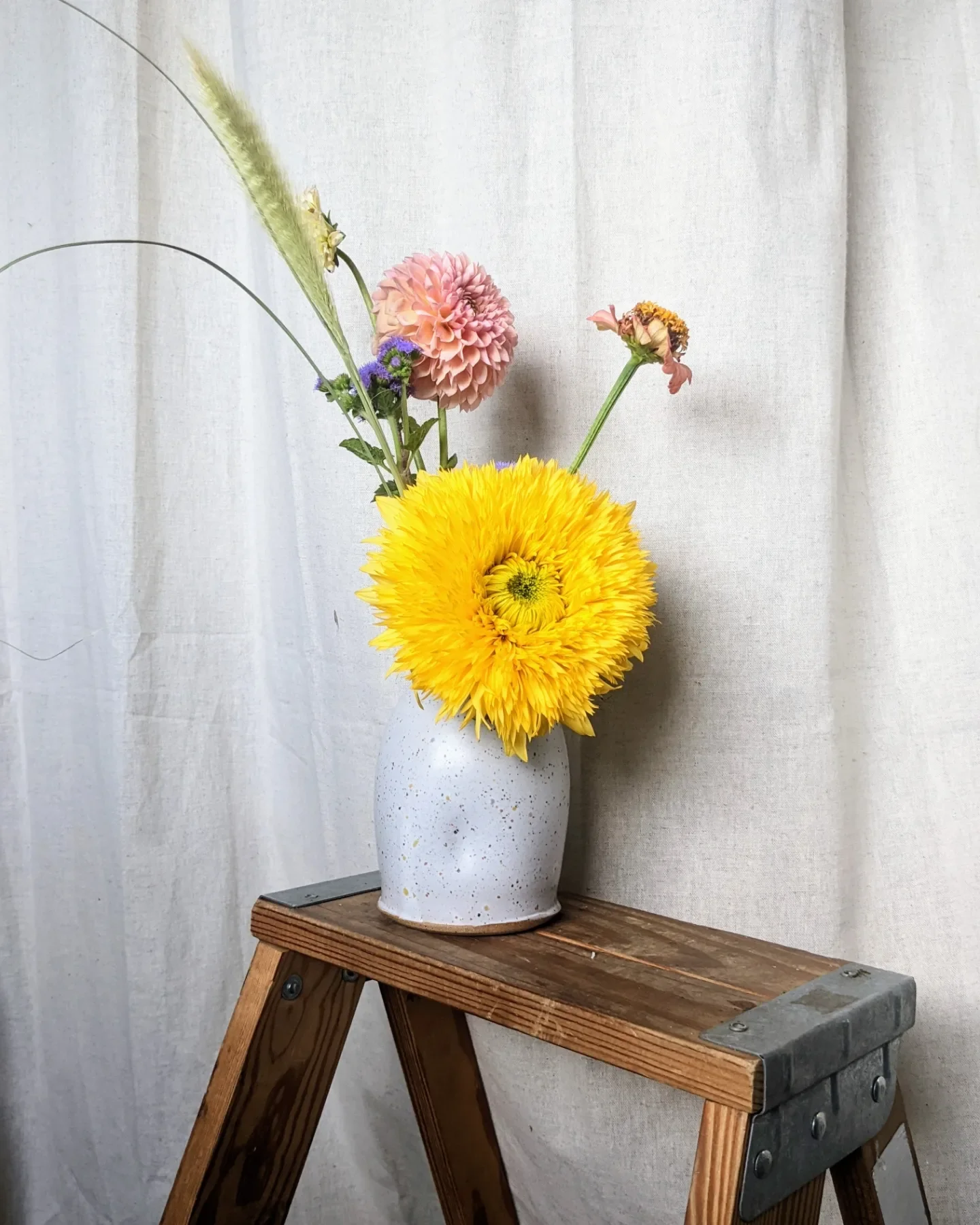  Petite arrangement in simple ceramic vase featuring big whimsical yellow flower and smaller pink and purple blossoms  