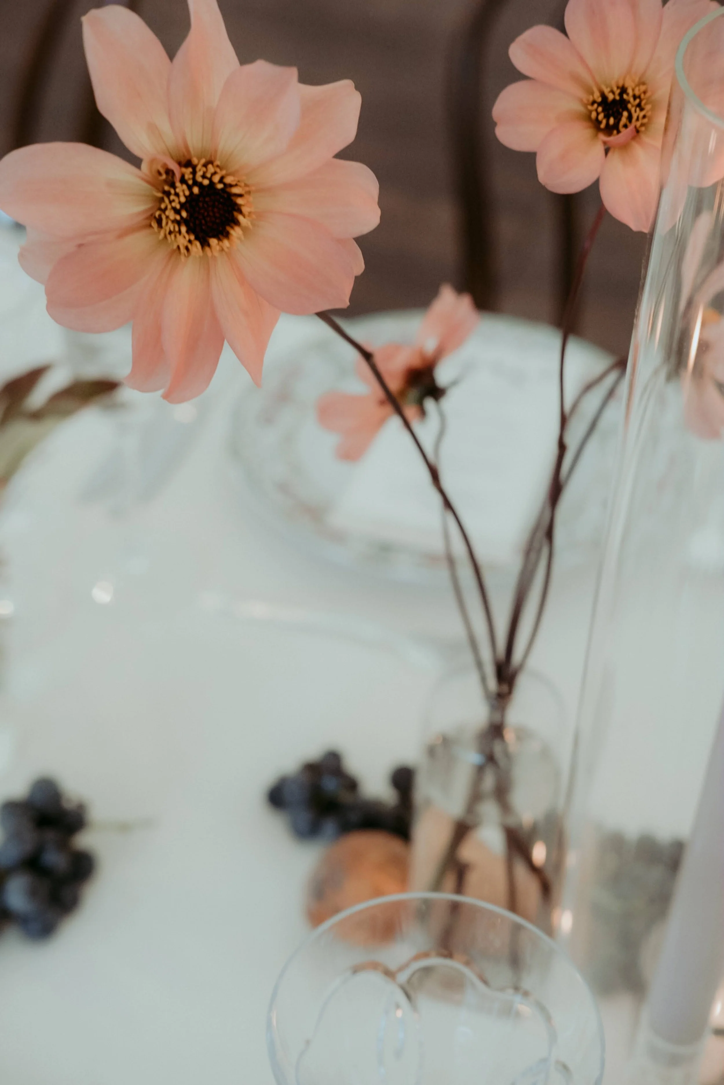  dainty pink dahlia stems without any foliage sit on wedding table in simple glass vessel 