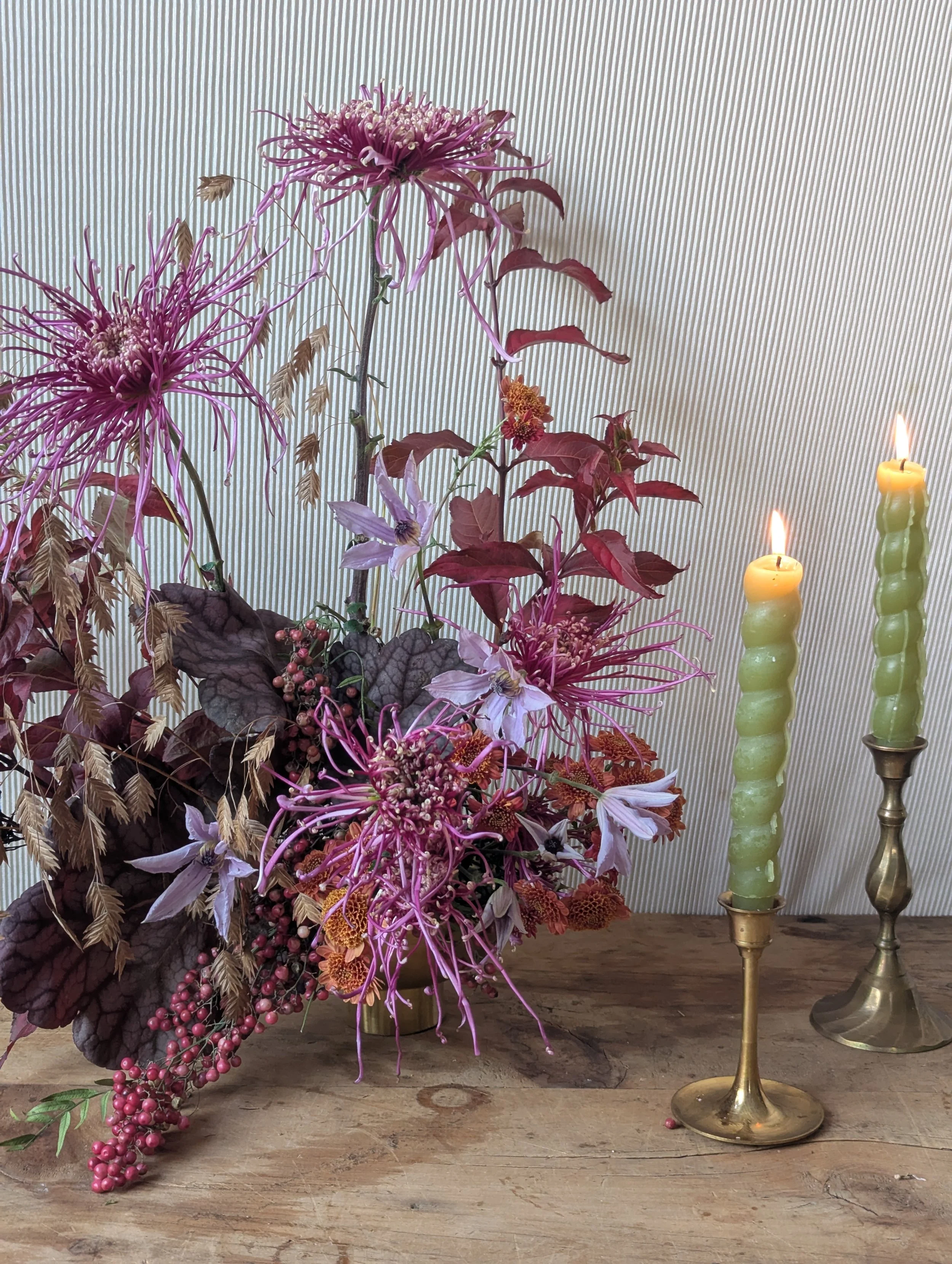  unique and airy petals on purple toned arrangement next to twisted green candles on brass holders 