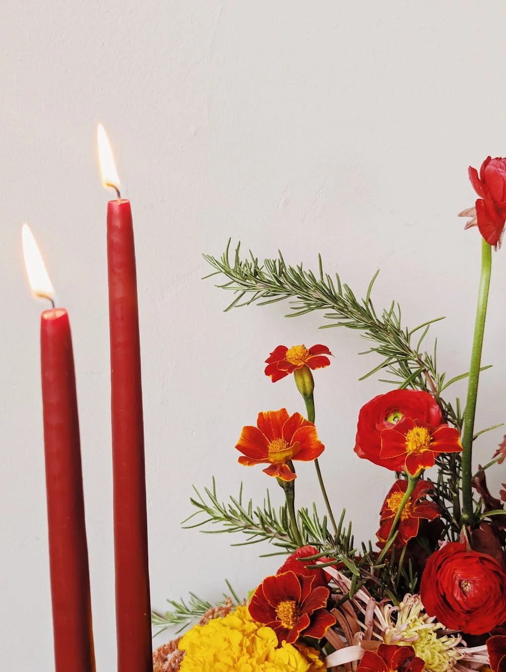  Lush floral arrangement with vibrant red blooms, delicate rosemary leaves and two bright red candlesticks 