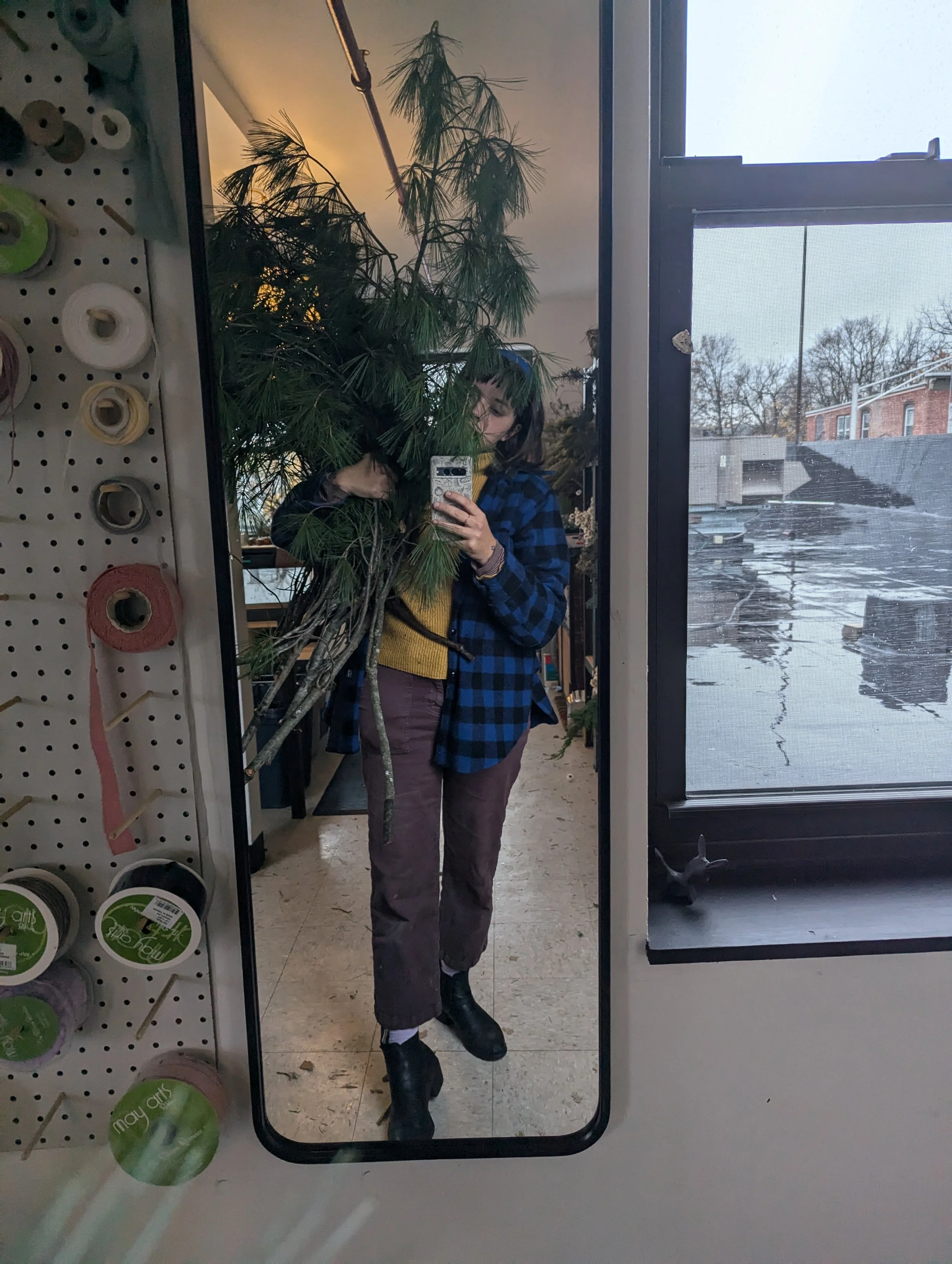  Sustainable floral designer holding tall, freshly collected evergreens  