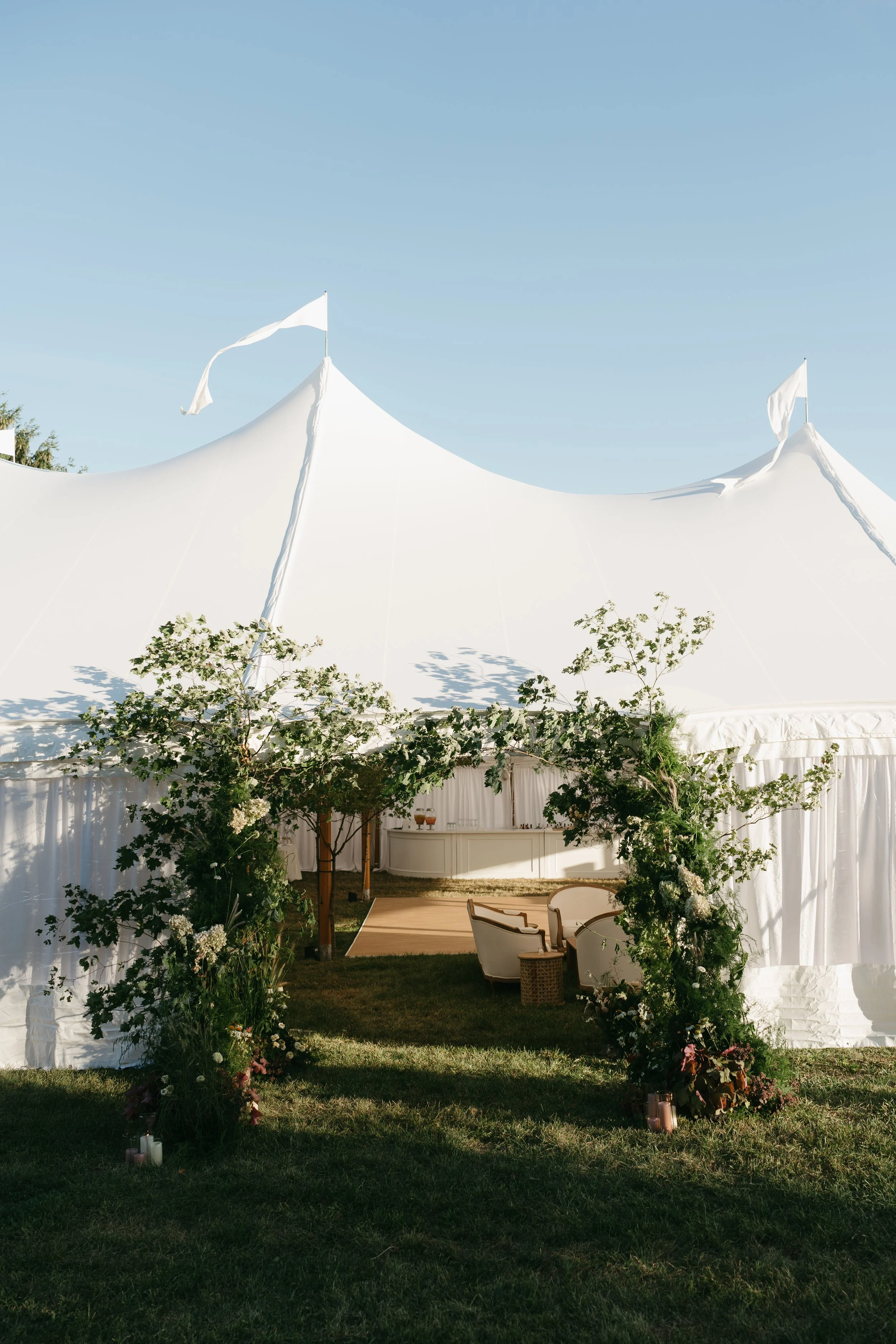 Floral-covered tent entrance with climbing greenery, meadow flowers, and candle clusters at a Pine Plains private residence wedding