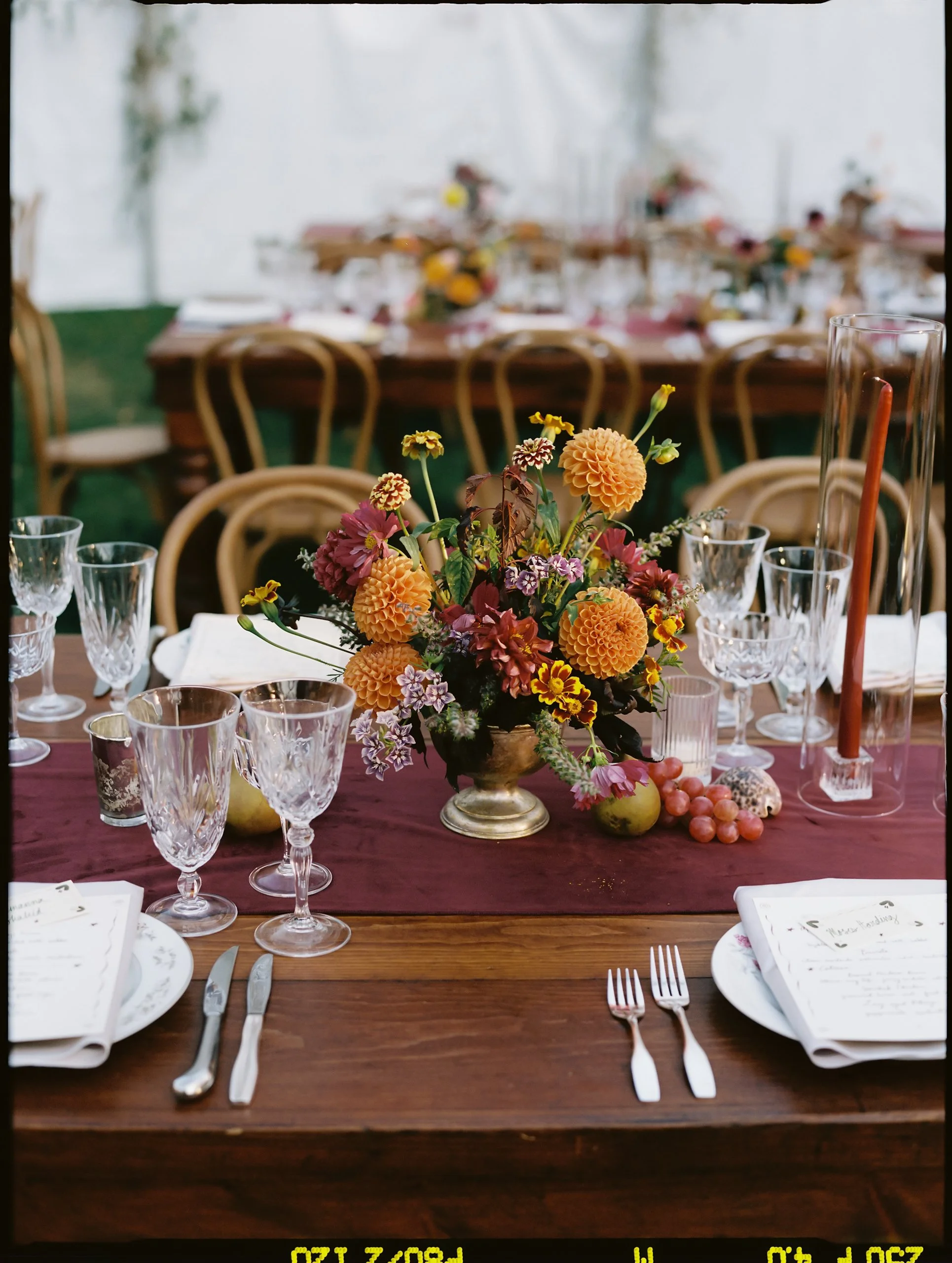 Fall table centerpiece featuring dahlias, marigolds, and textured blooms arranged on a wine-toned runner