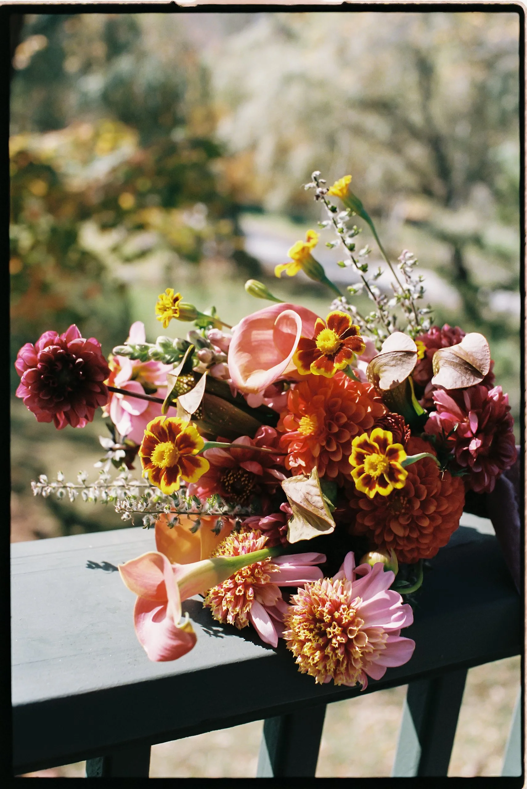 Autumn bridal bouquet with dahlias, calla lilies, and marigolds resting on a painted railing at Deer Mountain Inn