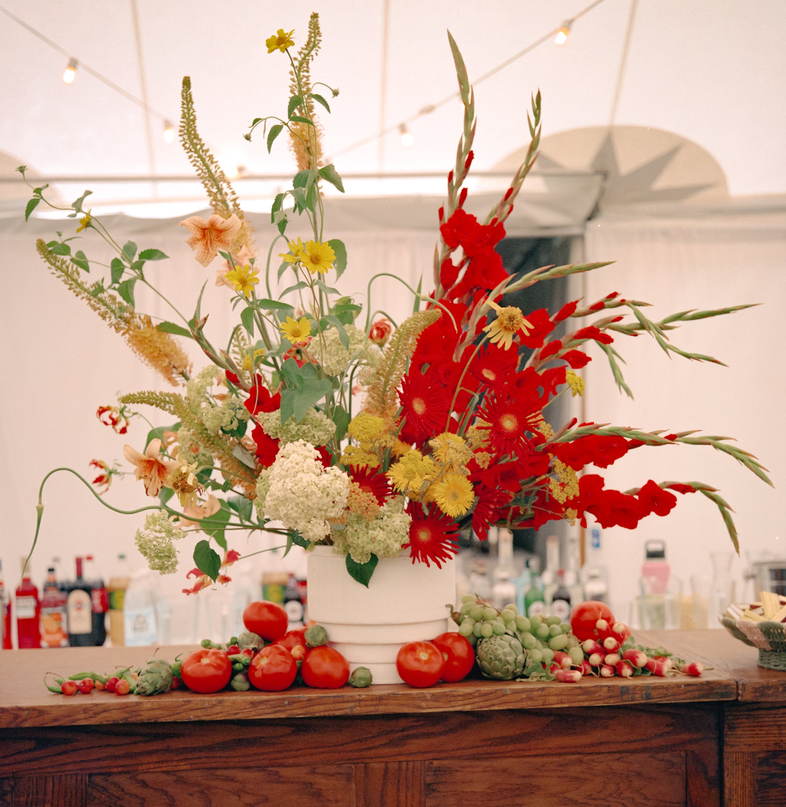Bold floral arrangement with red gladiolus, yellow blooms, and seasonal flowers styled on bar at private estate wedding