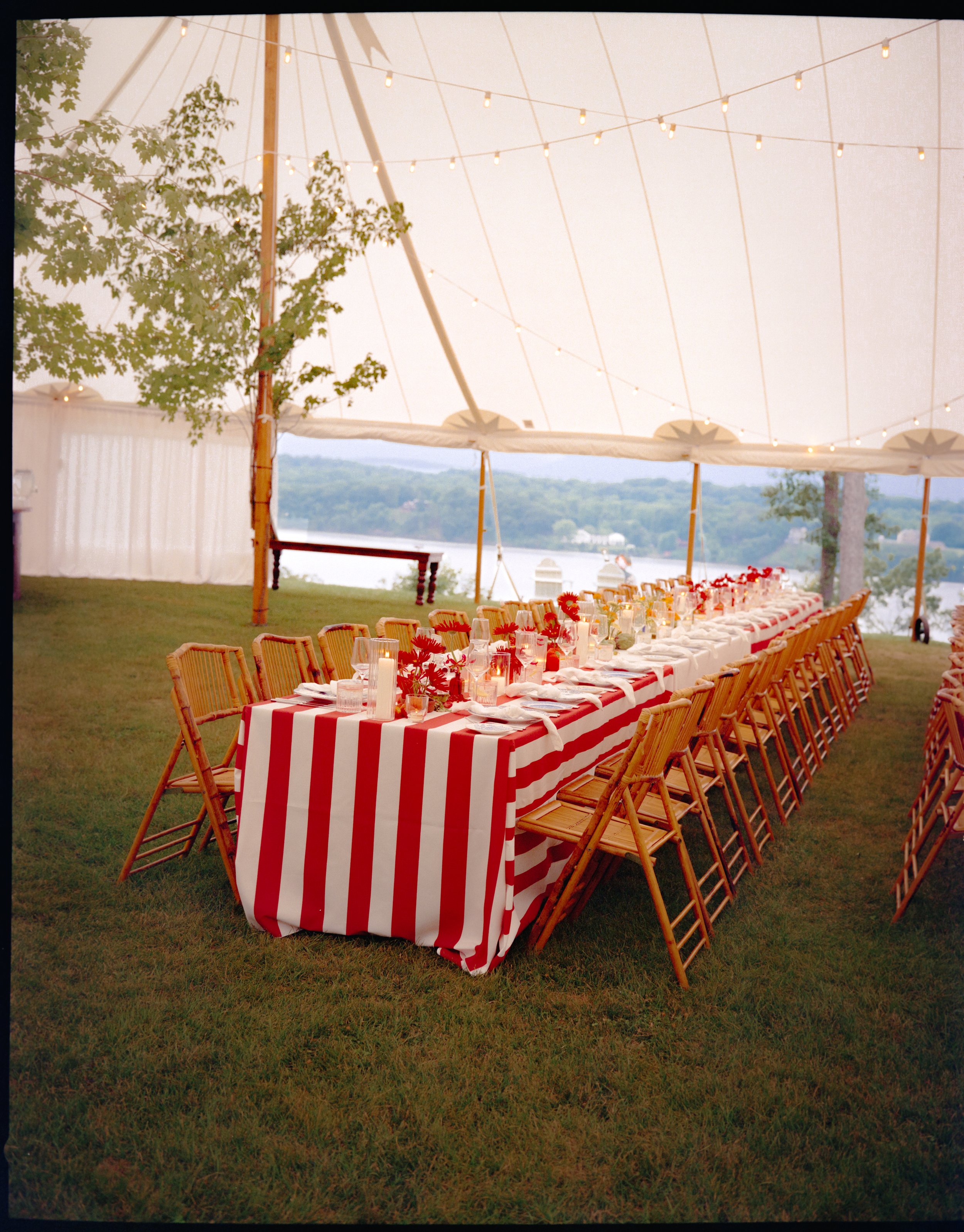 Long banquet table with red-and-white striped linens under sailcloth tent