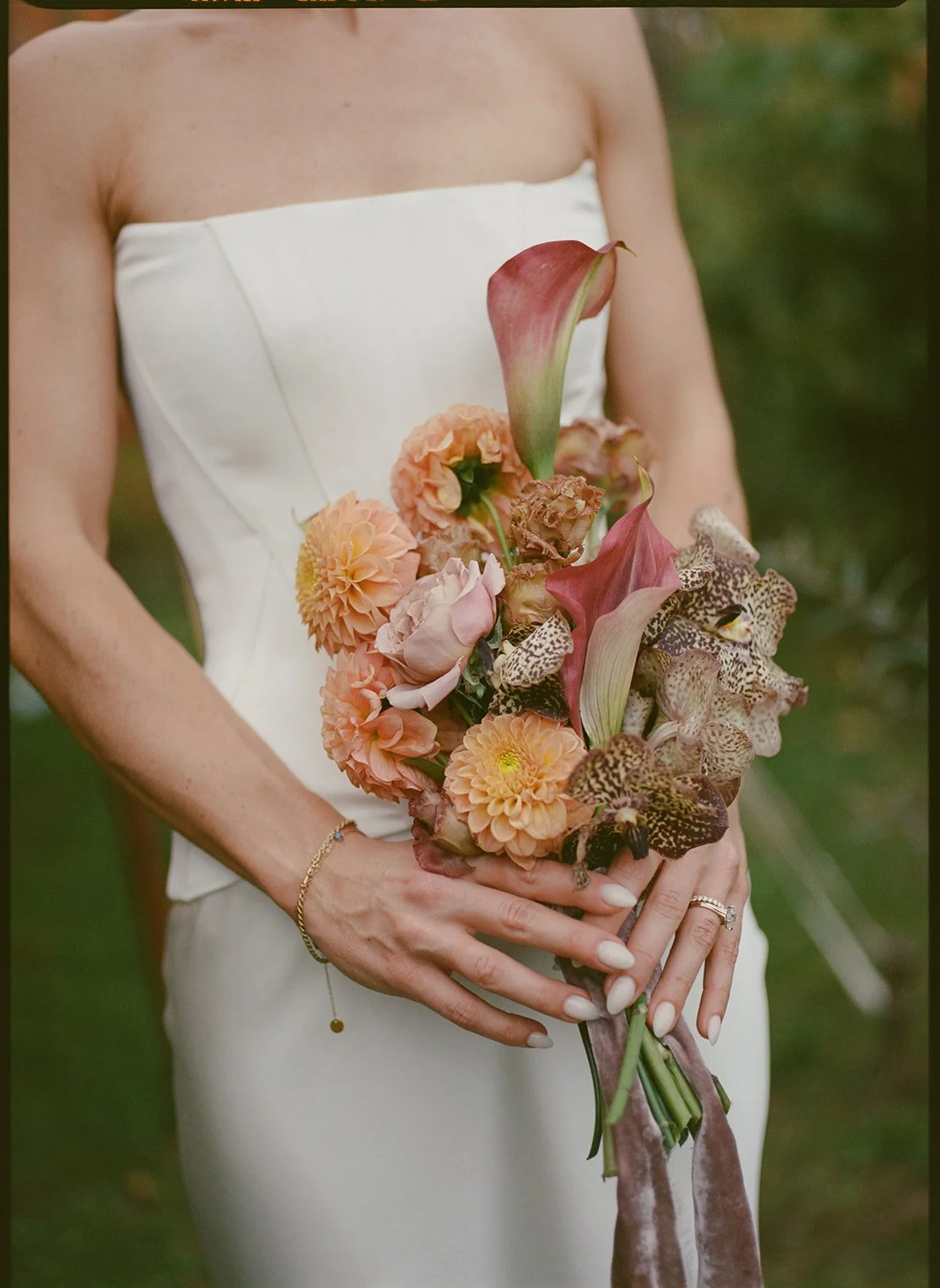 Bride holding an airy, autumn bouquet with dahlias, calla lily, and textured foliage in warm, muted hues.