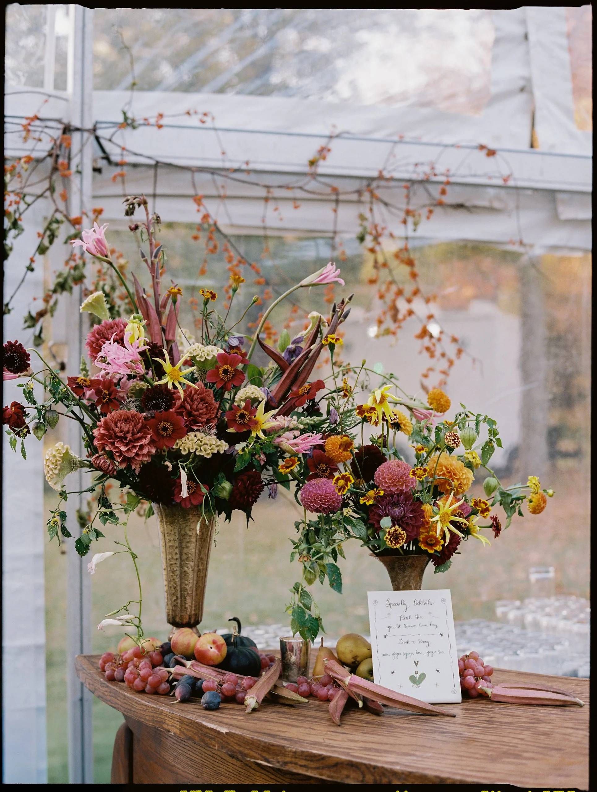 Statement floral arrangement overflowing with autumn dahlias, marigolds, and textural foliage styled on a wooden welcome table